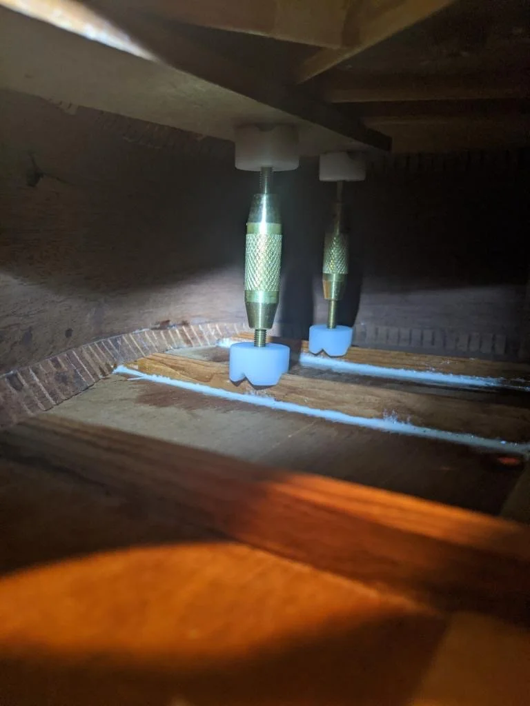 Close-up of a mechanical device inside a wooden furniture piece, with metal components and plastic parts, possibly part of an adjustable mechanism or hardware assembly.