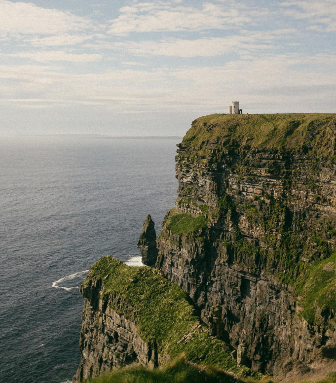 Cliffside overlooking the ocean with a small white building on top of the grassy cliff.