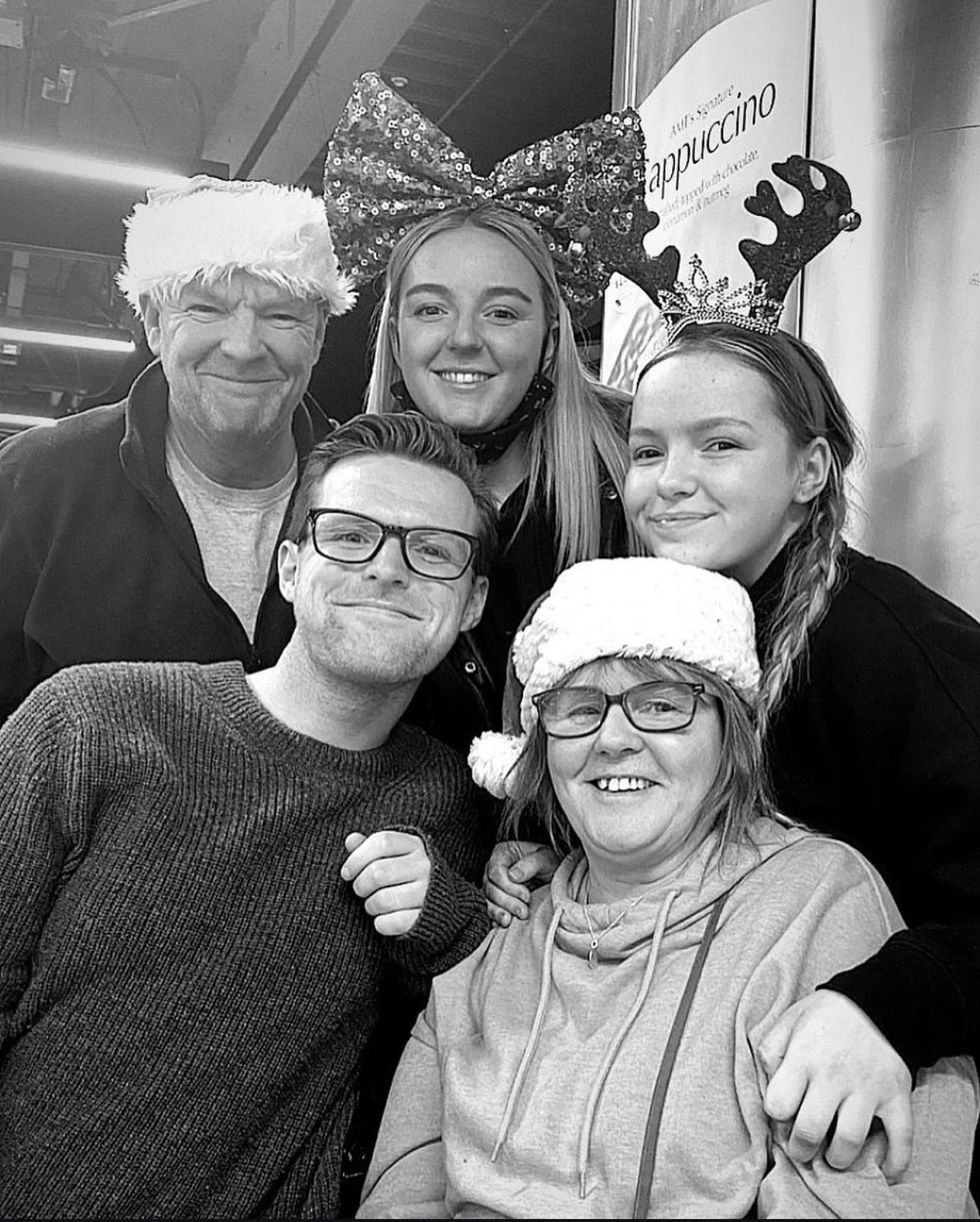 Group of six people dressed in holiday costumes, including Santa hat, reindeer antlers, and Christmas hats, celebrating Christmas together.