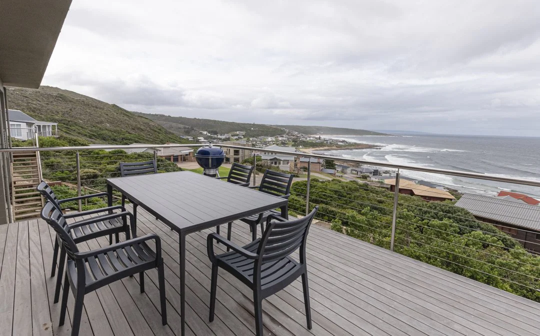 Outdoor balcony overlooking the ocean with a dining table, six chairs, and a barbecue. Perfect for watching the sunset or sunrise or a braai.