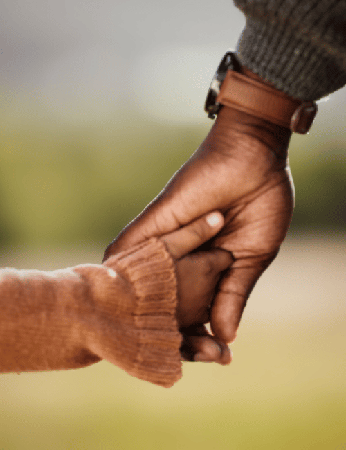Close-up of an adult and child's hands holding each other outdoors.