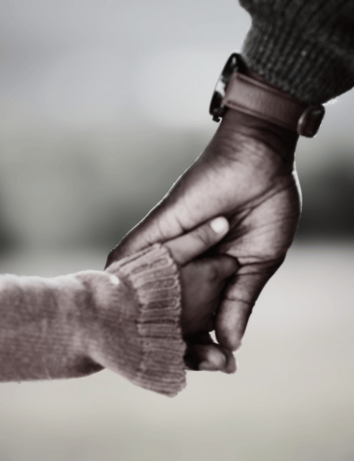 A close-up of a larger hand holding a smaller child's hand, showing a tender moment.