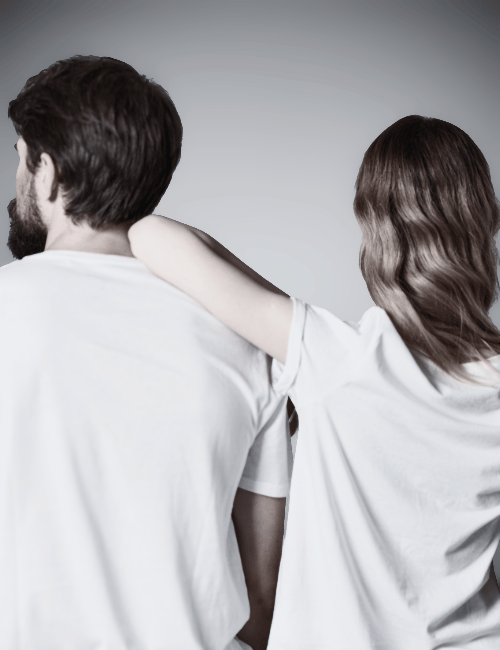 A woman with wavy hair puts her arm around a man with a beard, both seen from the back, wearing white T-shirts.