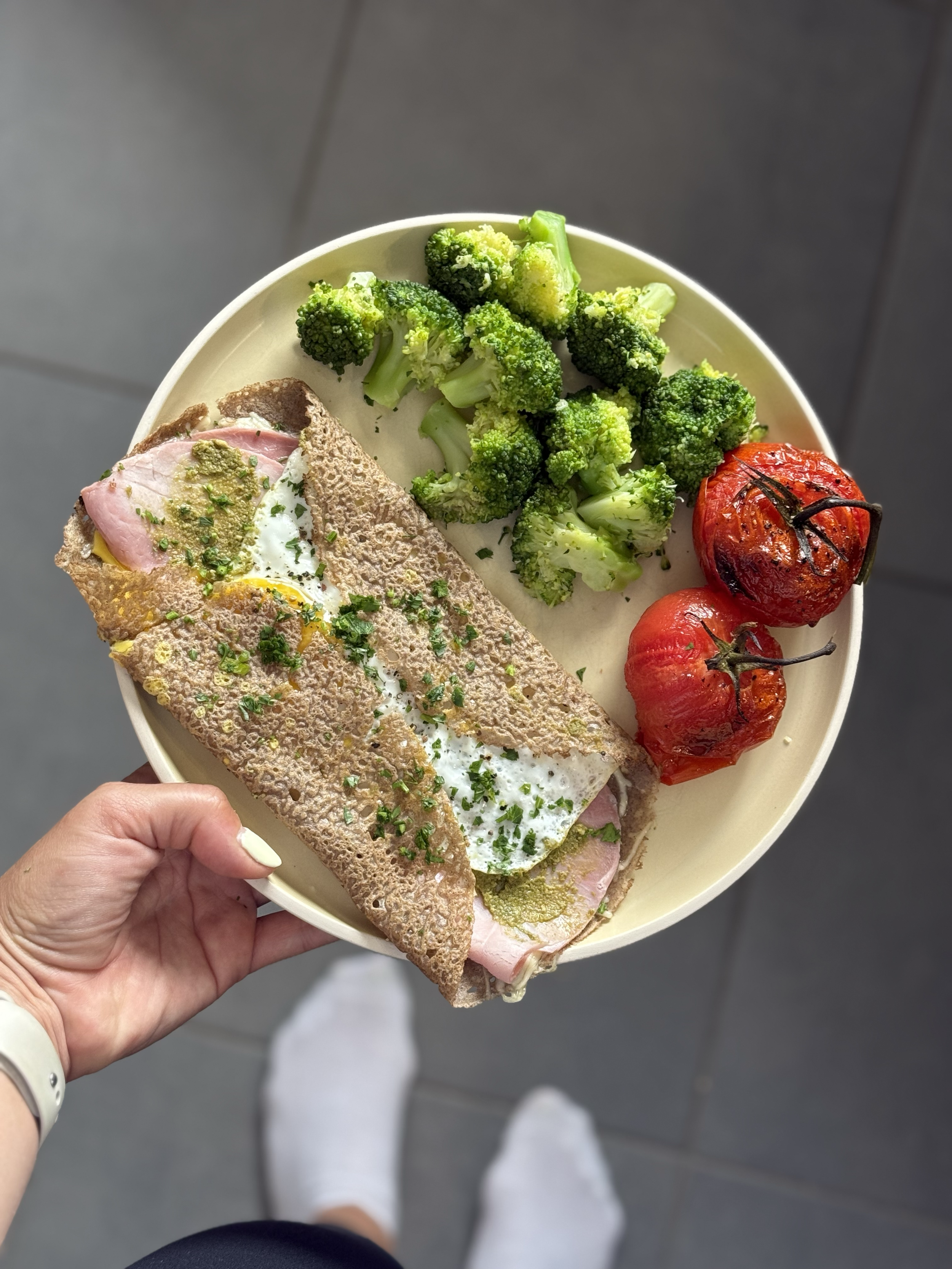 A plate with grilled tomatoes, broccoli, and a sandwich with egg, ham, and green sauce.