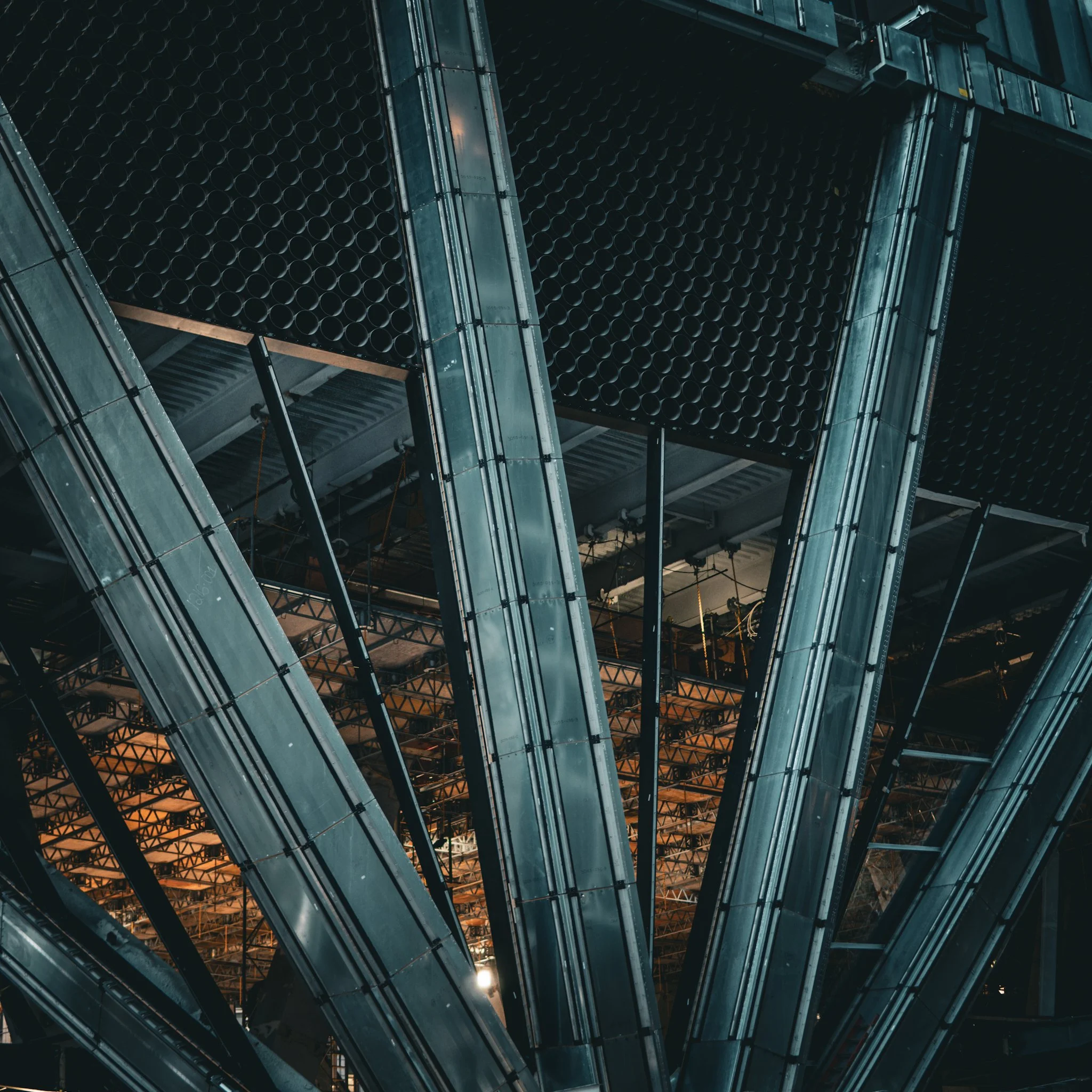 View of the underside of a modern steel and glass building with multiple levels and architectural details visible.