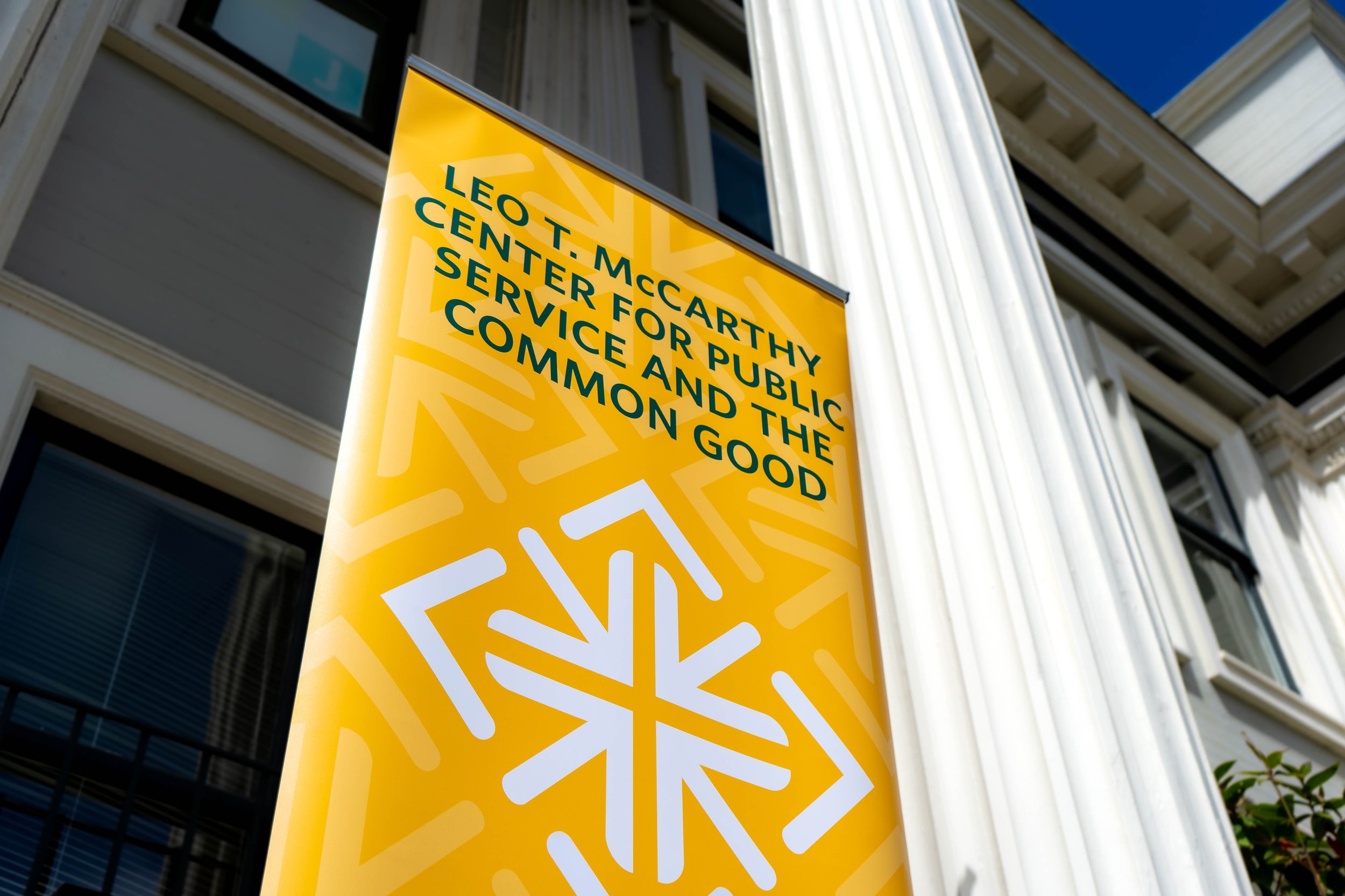 Yellow banner with blue text reading 'Leo T. McCarthy Center for Public Service and the Common Good' in front of a building with white columns.