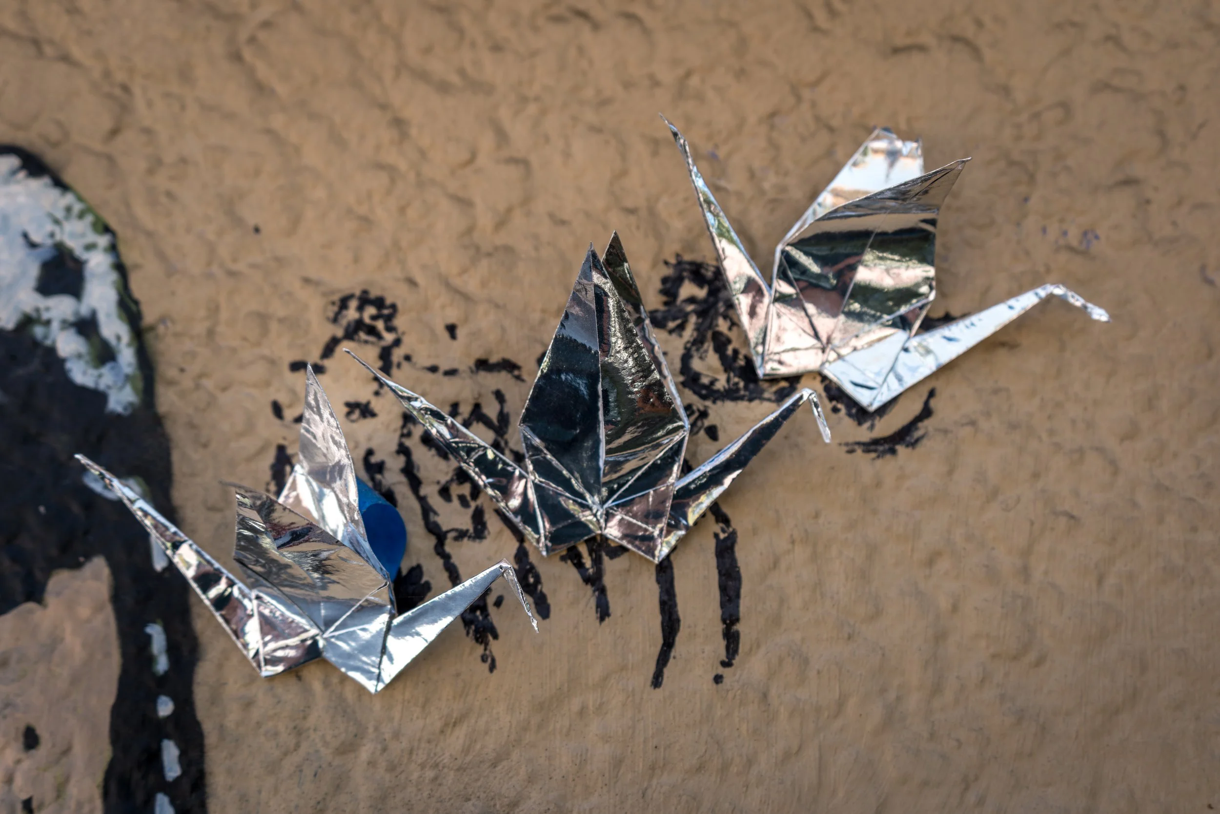 Origami butterflies made of shiny silver foil paper arranged on a brown textured surface with black ink drawings.