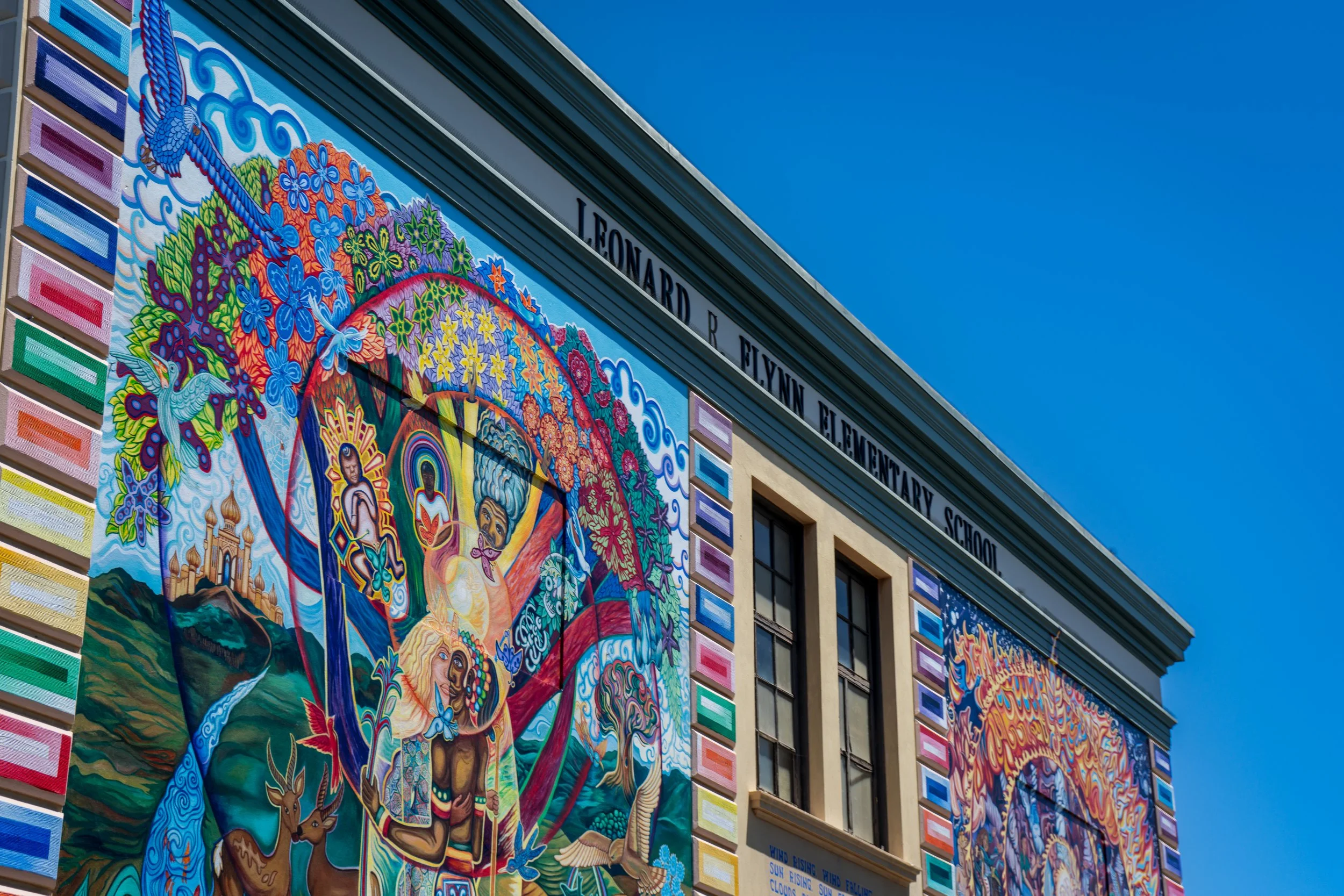 Colorful mural on a building exterior with deers, humans, trees, and vibrant patterns, part of Leonard R. Flynn Elementary School