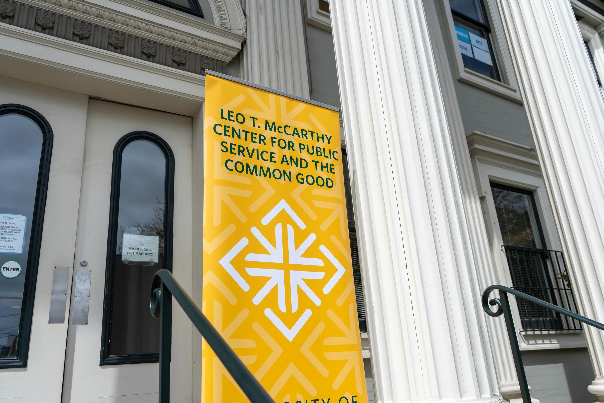 Yellow banner outside a building with white columns, displaying the text: 'Leo T. McCarthy Center for Public Service and the Common Good'.