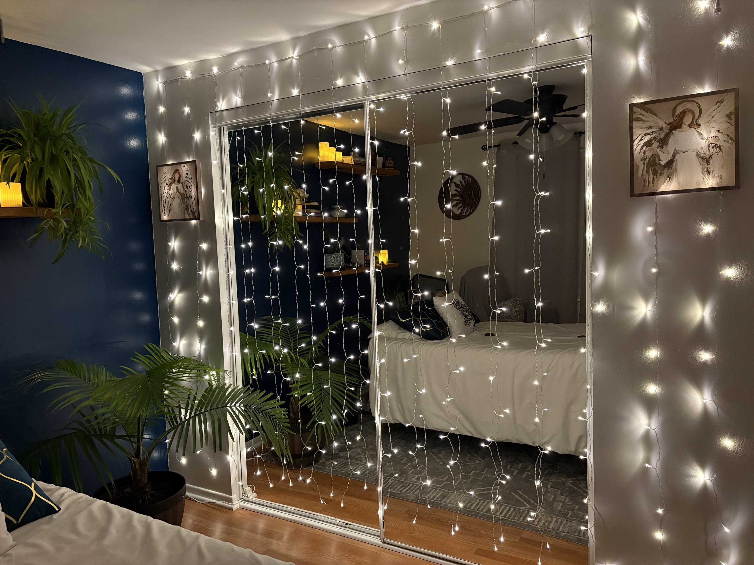 Ascension Healings energy healing reiki QHHT Living room with a large mirror decorated with string lights, a blue wall, a houseplant, and framed artwork on the wall.