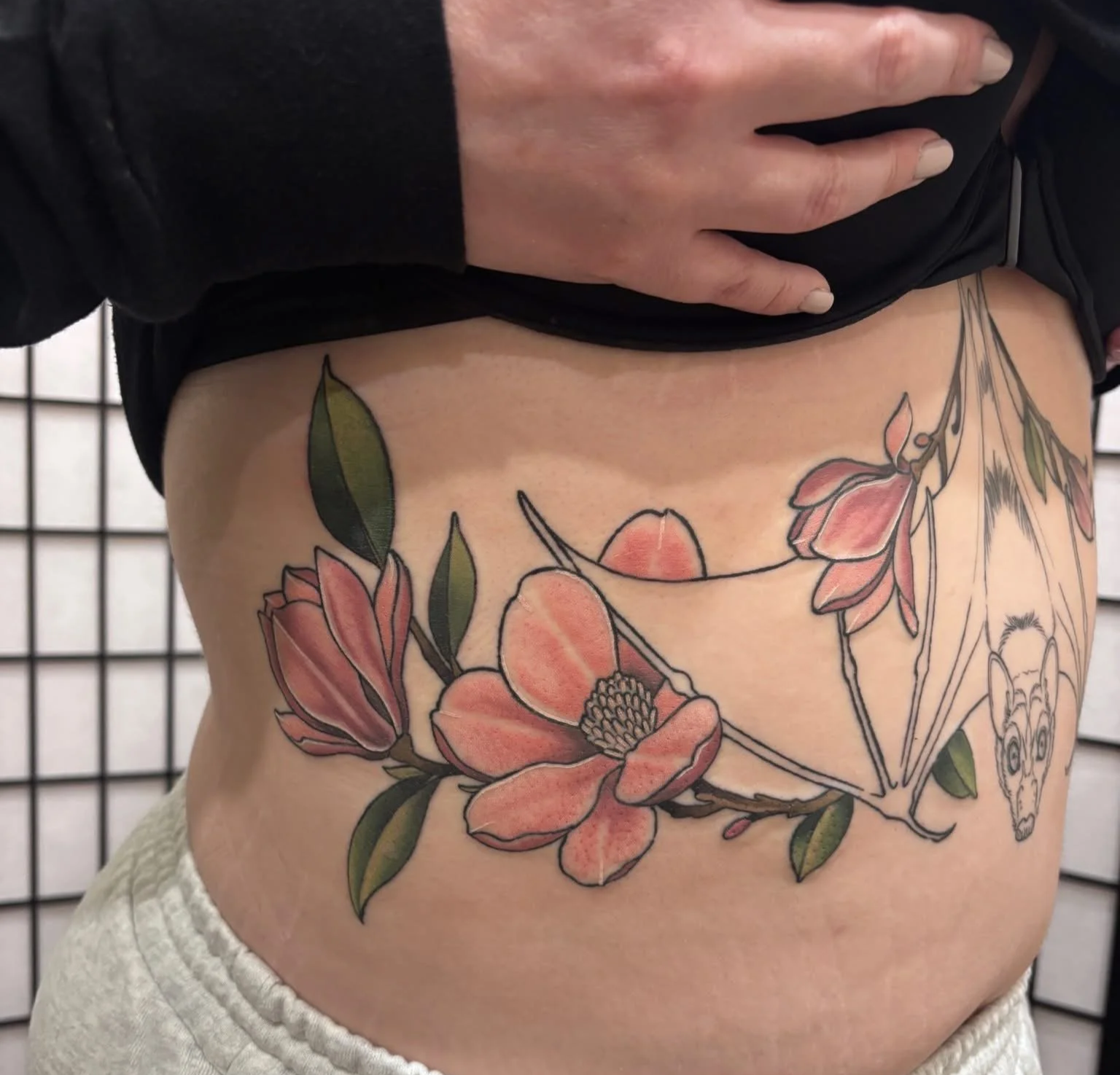 Large bat sternum tattoo with magnolias, designed to flow across the stomach and chest in a dark feminine neo-traditional style