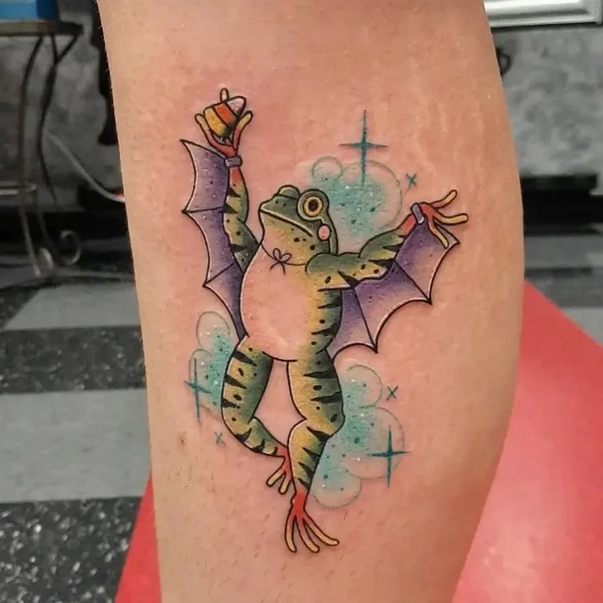 Whimsical frog tattoo with bat wings and candy corn in a playful neo-traditional style