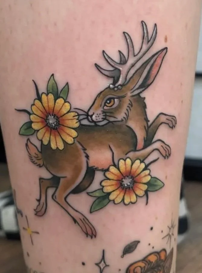 Neo-traditional jackalope tattoo with daisies, detailed antlers, and soft botanical shading