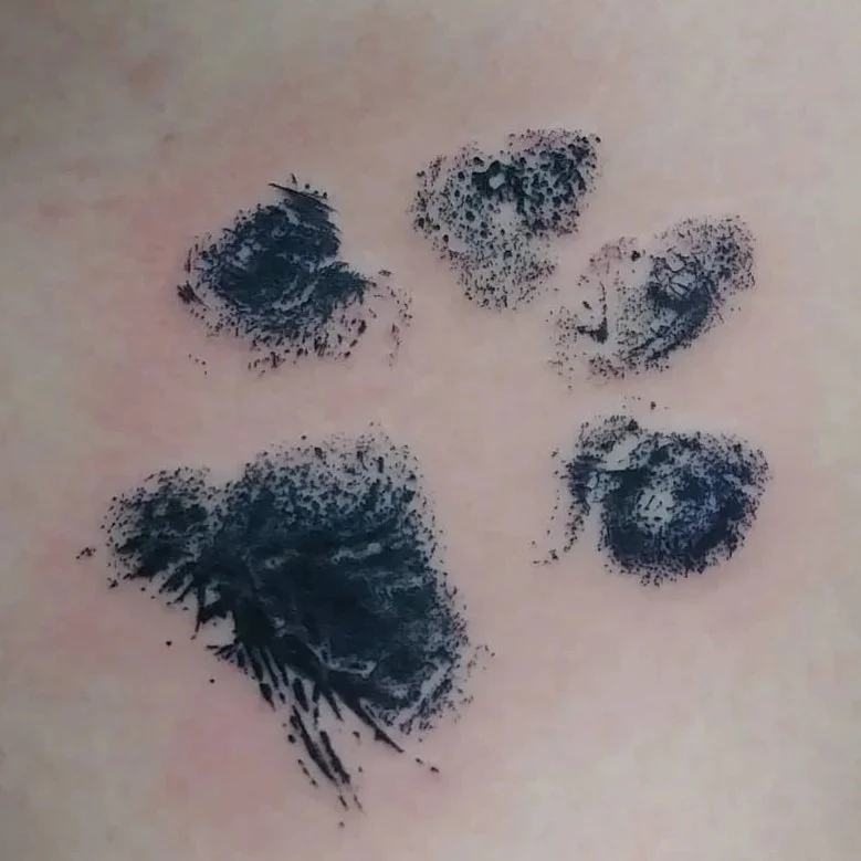Simple pet paw print tattoo with clean linework and soft black and grey shading