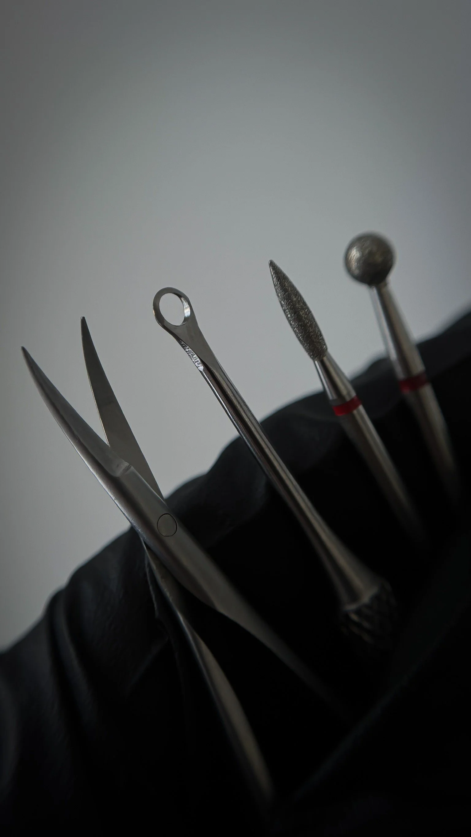 Set d'outils de manucure, comprenant des pinceaux et des outils en acier inoxydable, tenu par une main gantée noire.