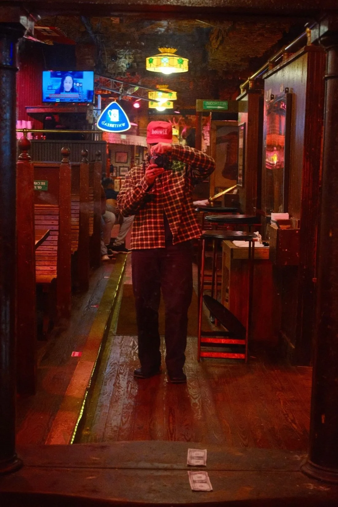 OrlandoVaughn taking a photo of himself in a mirror inside a dimly lit restaurant or bar with wooden decor, hanging lights, and neon signs.