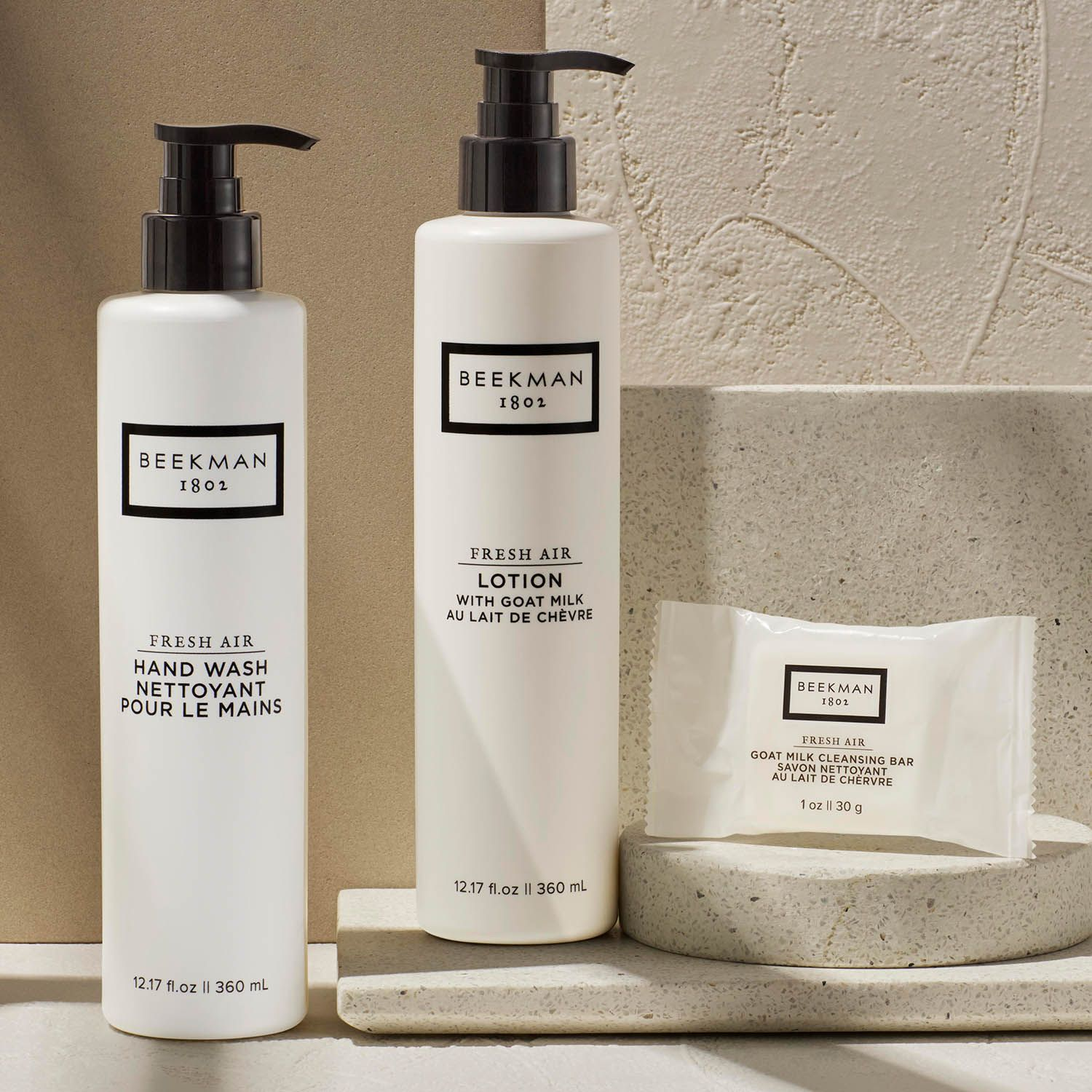 Three Beekman skincare products including hand wash, lotion, and cleansing bar displayed on a neutral-colored surface with textured background.