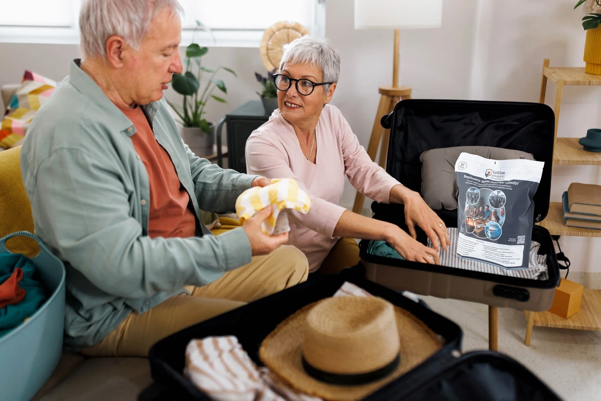 An elderly couple packing a suitcase, with the woman helping to put in a medical supply bag, in a bright living room.