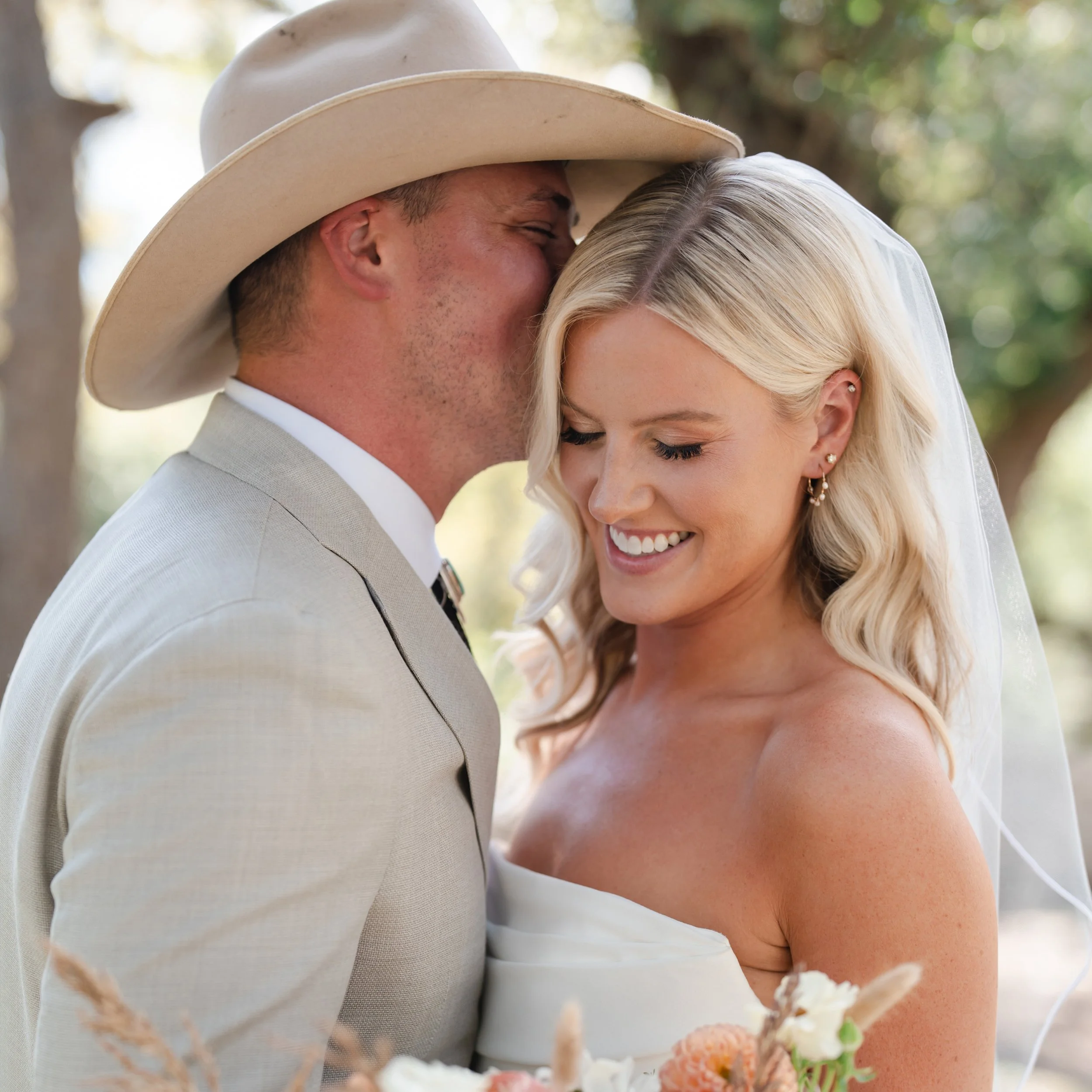 Documentary style wedding film moment of a groom in a cowboy hat kissing his bride at a Hill Country wedding