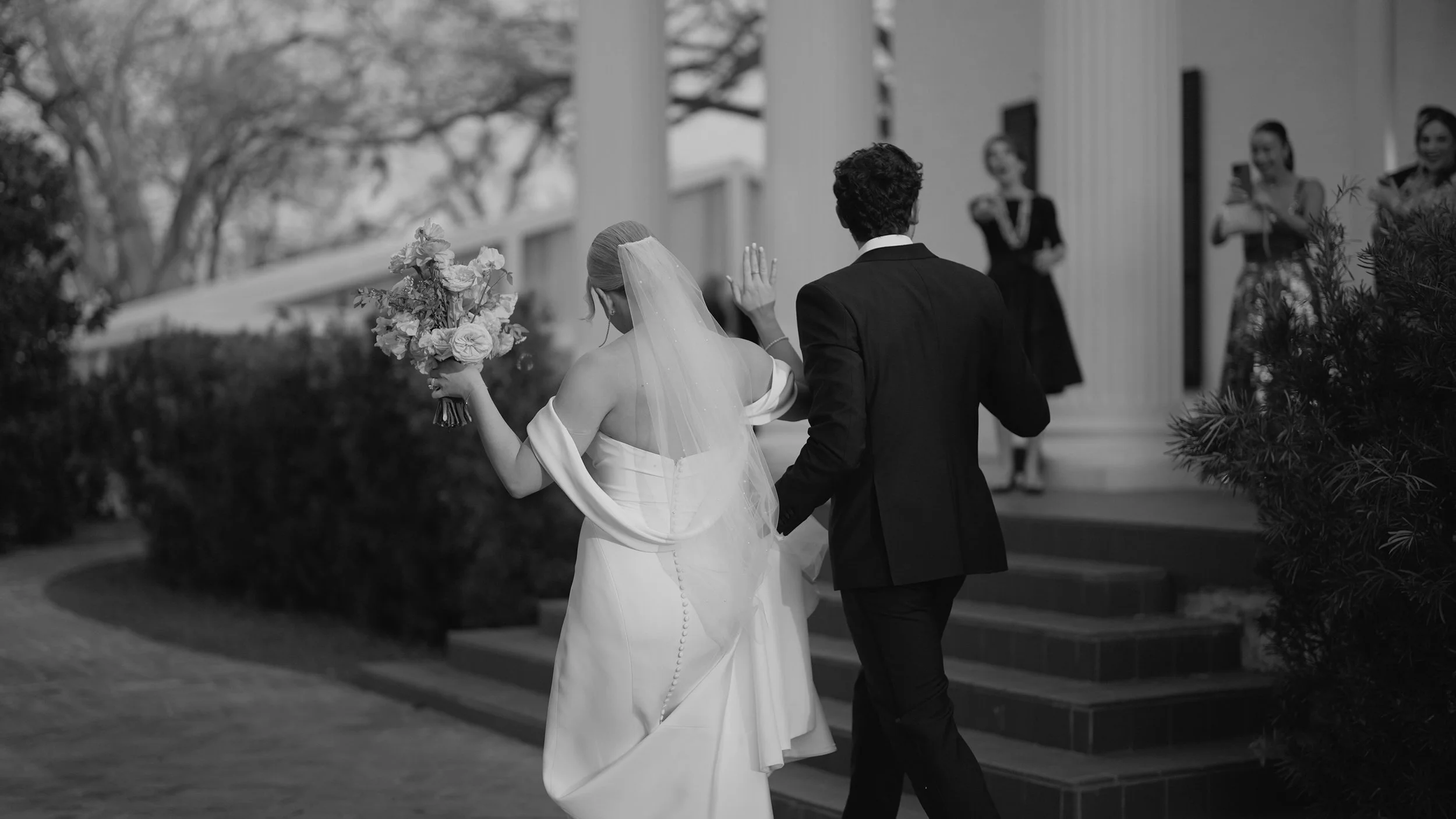 Black and white Austin wedding photography of a bride and groom walking together with bouquet and veil