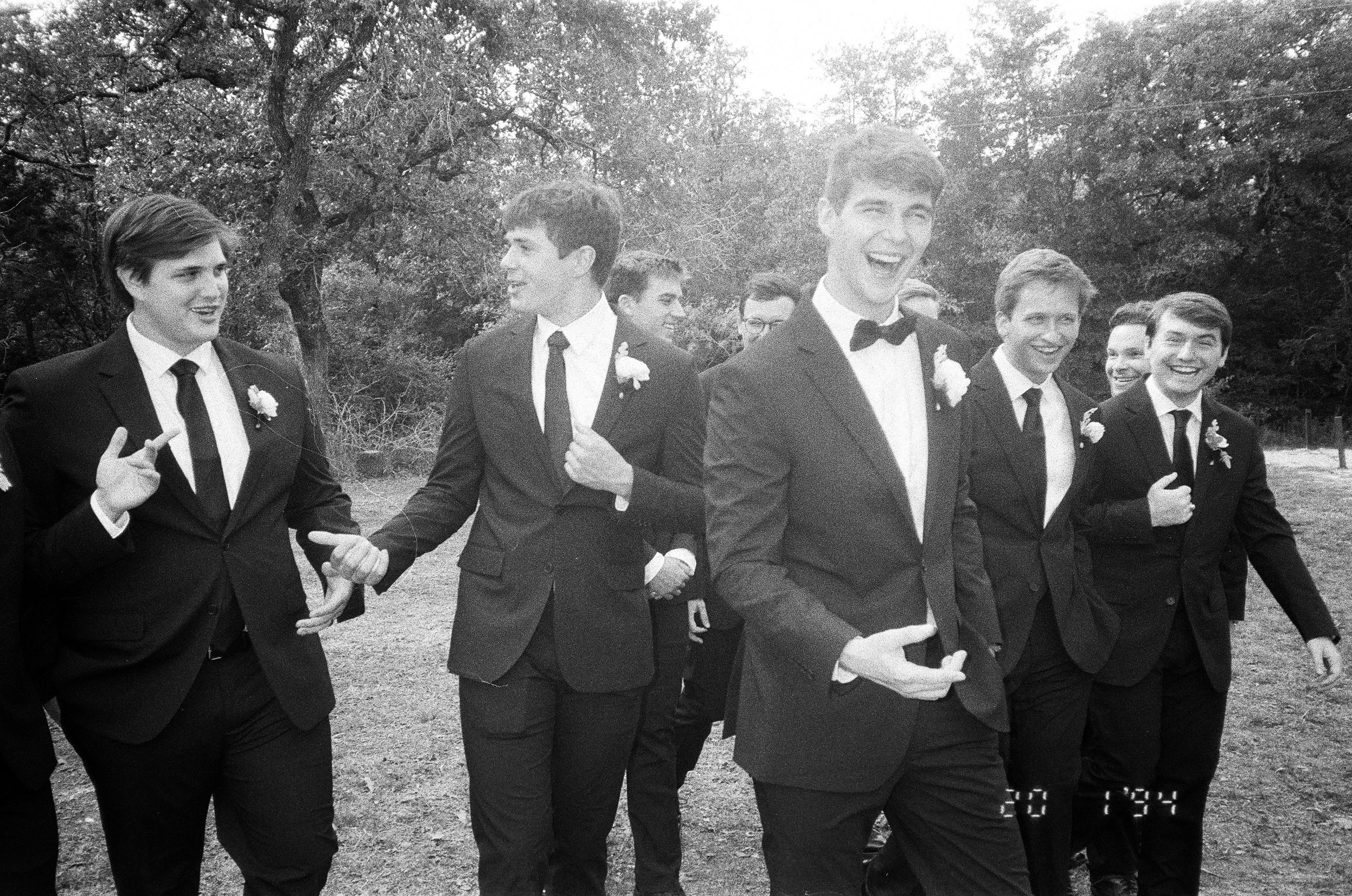 Candid black and white wedding photography of groomsmen laughing outdoors at a Central Texas wedding