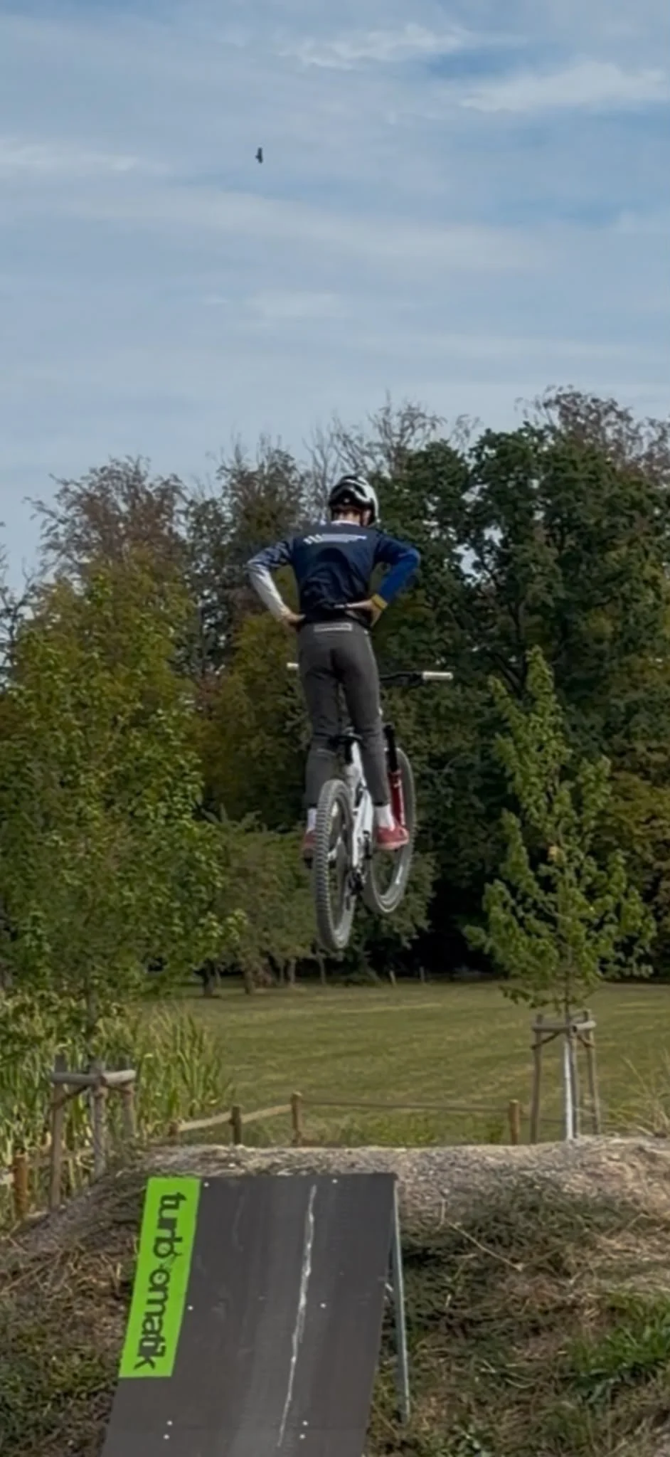 Ein Mountainbiker des Teams MR20 Karlsruhe fliegt mit massiver Airtime von einem TURBOMATIK Sprungelement im Bikepark Zavelstein, mit Wald und bewölktem Himmel im Hintergrund. Der Sprung zeigt die Höhe und Dynamik.