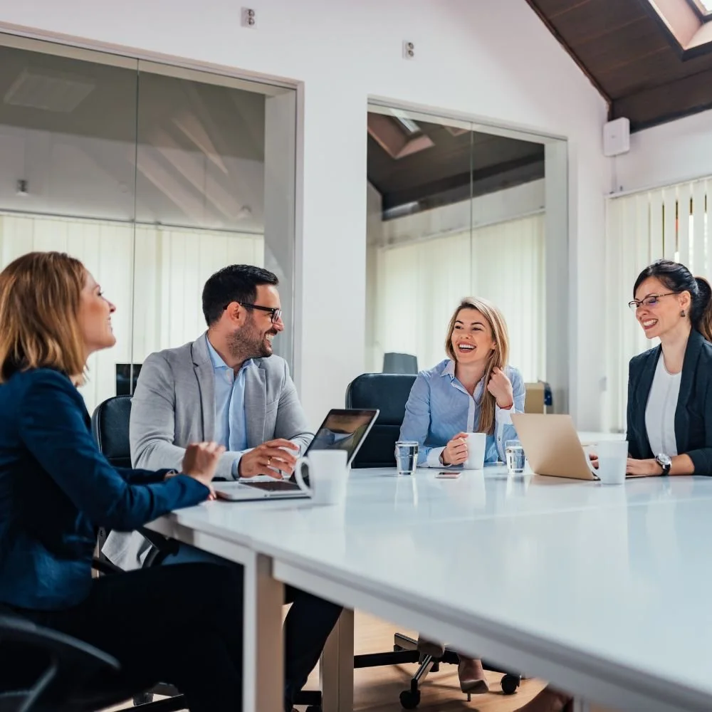 Four professionals sitting around a conference table, laughing and having a meeting in a modern office.