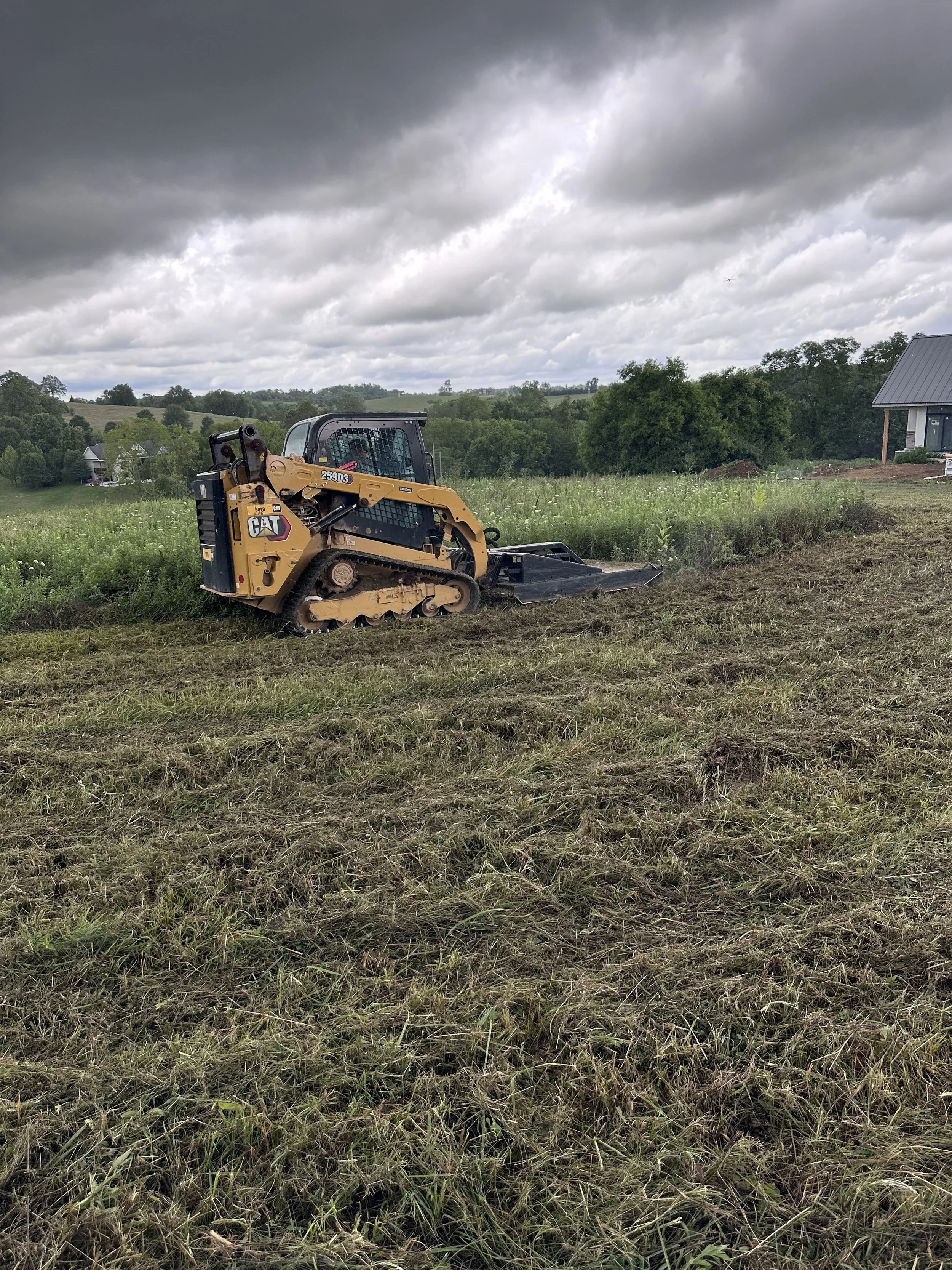 A small yellow Caterpillar bulldozer working on a grassy field under a cloudy sky.