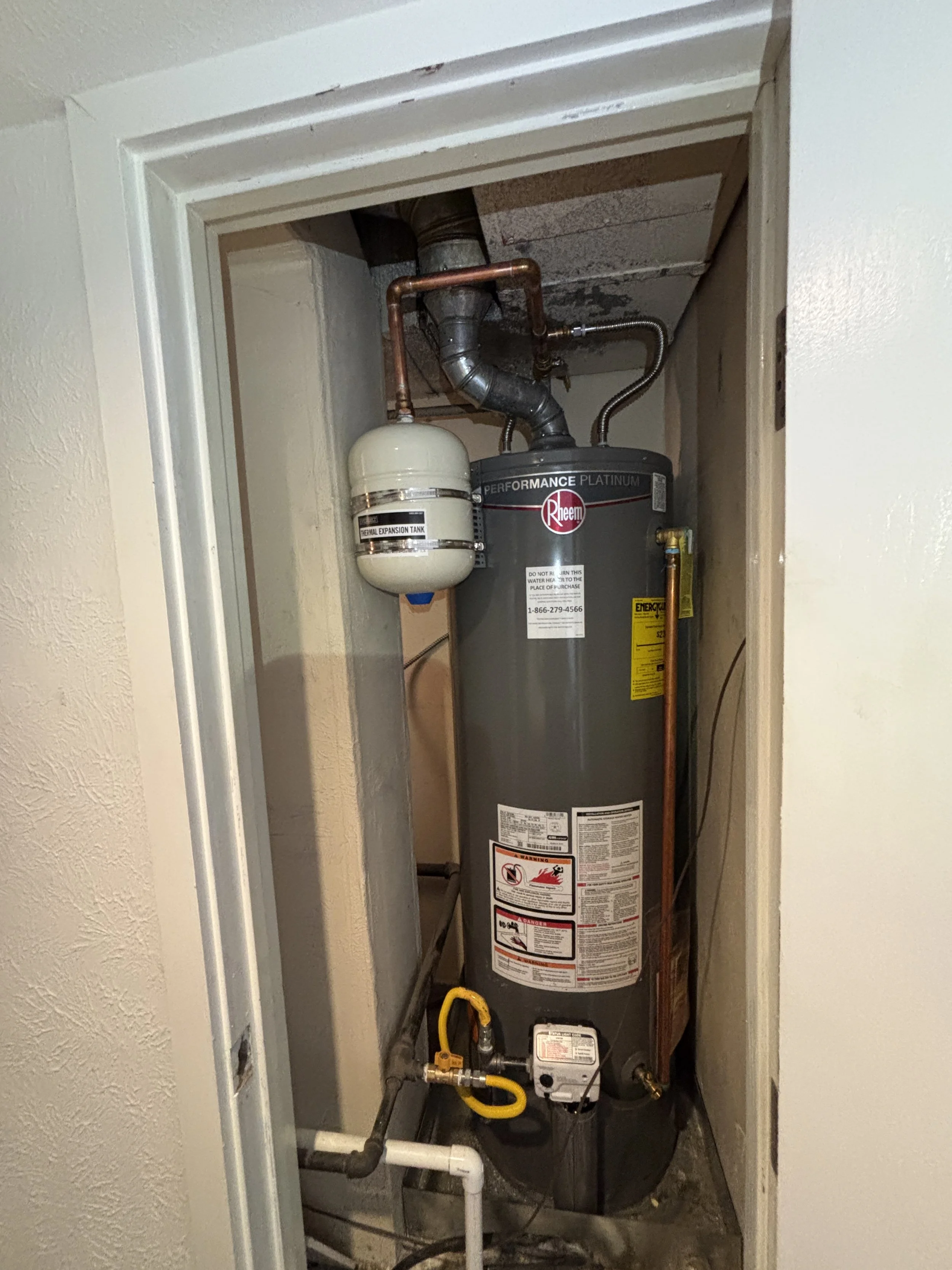An electrical water heater installed in an electrical closet with visible pipes, wires, and a temperature expansion tank.