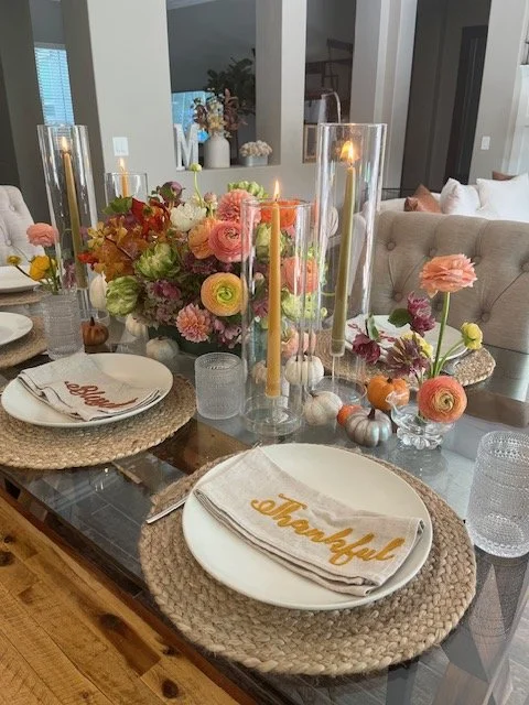 Decorated dining table with floral arrangements, candles, and place setting with napkin reading 'thankful' and 'bountiful'