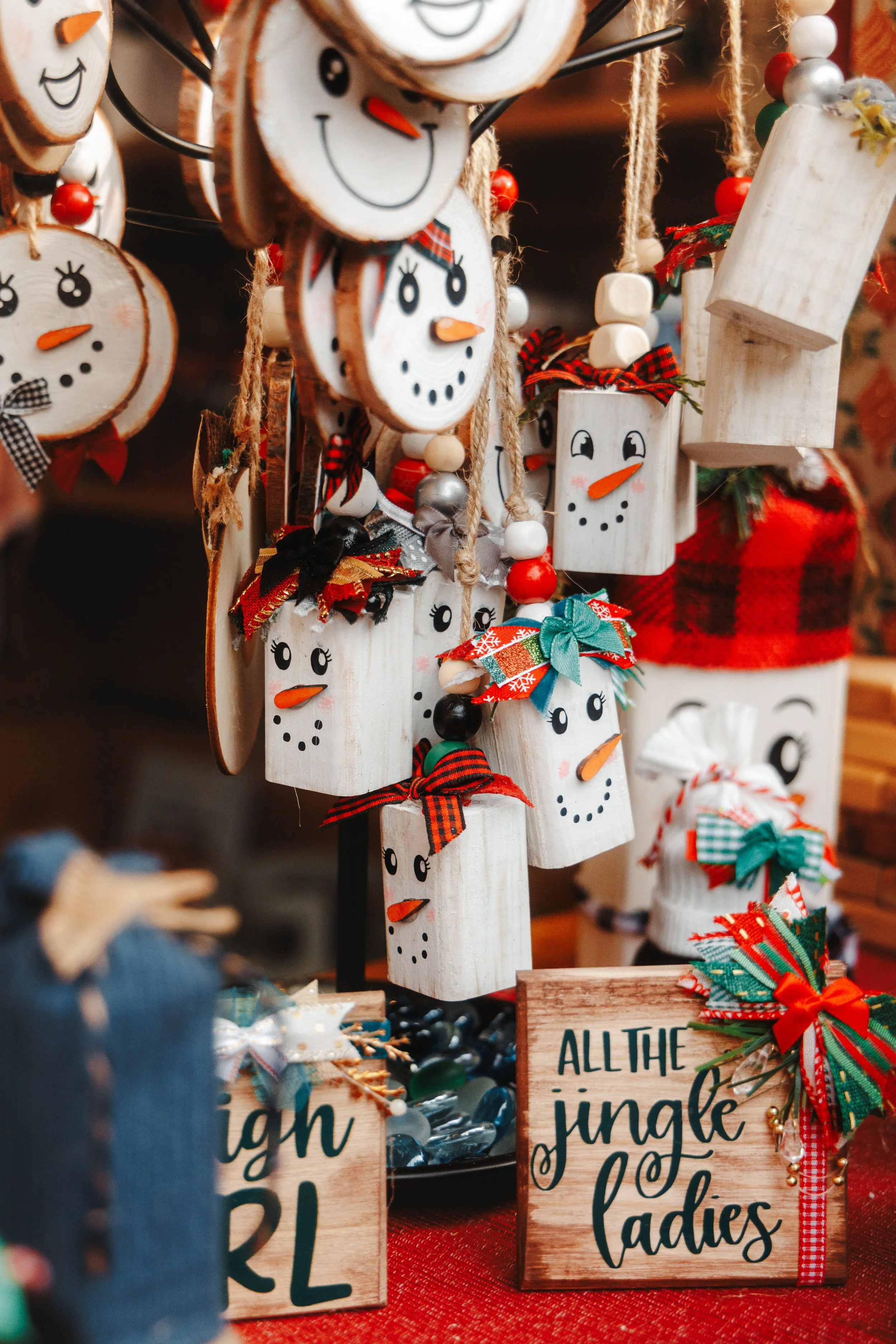 Handmade snowman and holiday decor on display at a craft fair, with signs reading 'All the jingle ladies' and other festive messages.