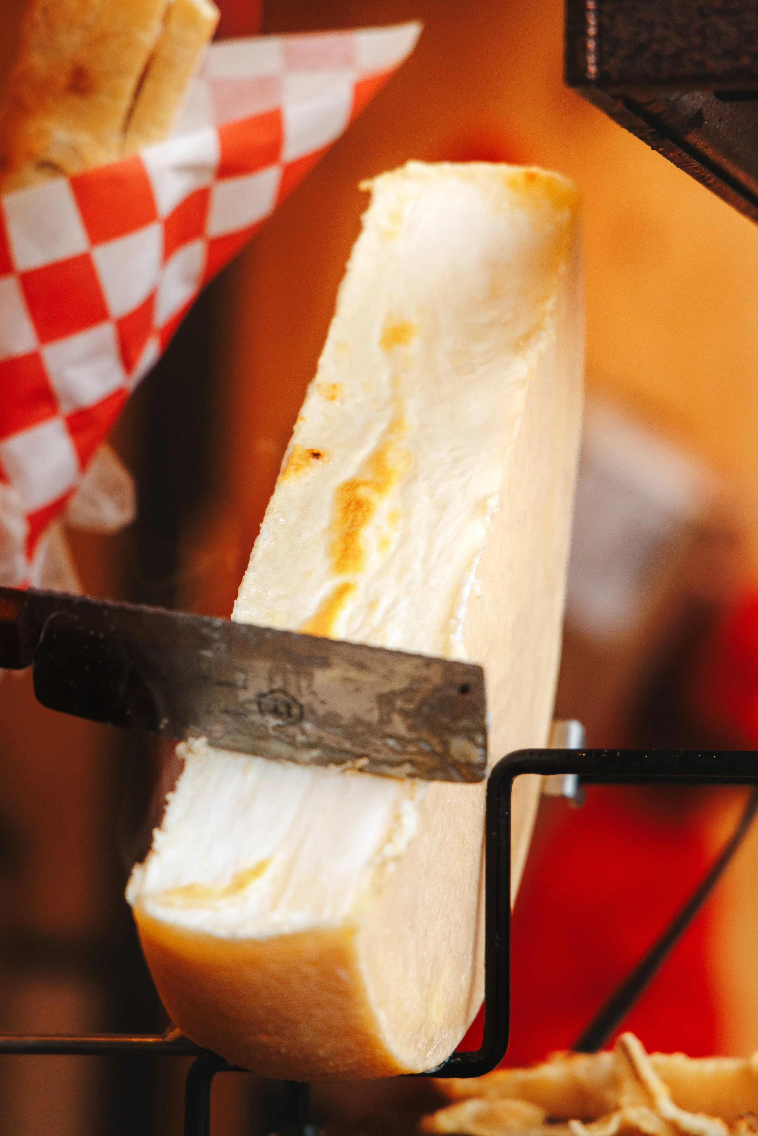 A large wedge of Swiss cheese being sliced with a cheese cutter on a wooden board.