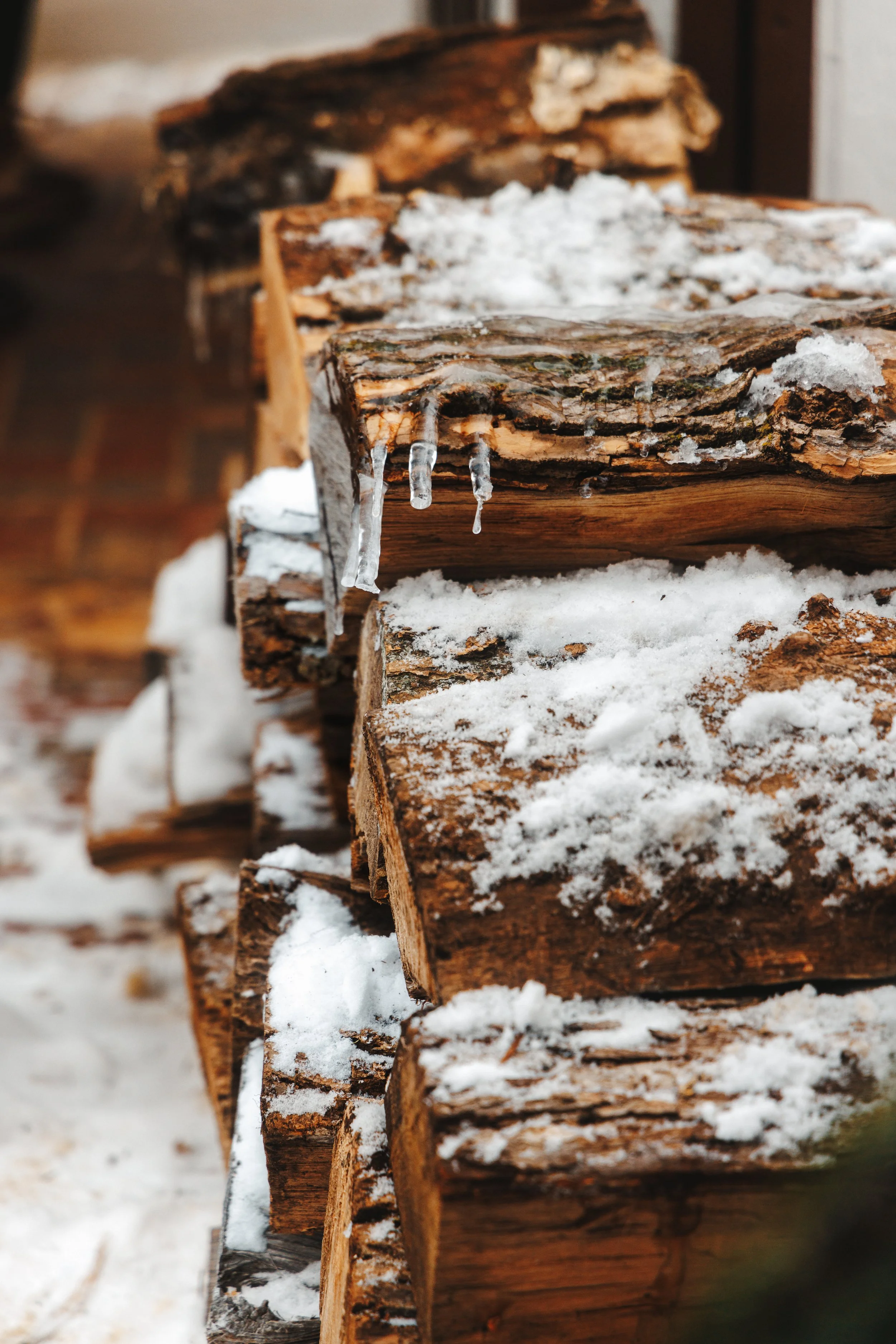Close-up of stacked firewood logs covered with snow and ice, with icicles hanging from the logs.