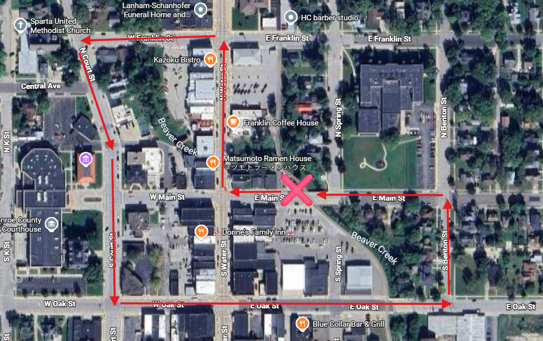 Map of a small downtown area with streets named W Main St, E Main St, E Oak St, and others. Red arrows illustrate a walking route starting at the southwest corner, going north on N S Kent St., then east on W Franklin St, north on N Court St., west on W Oak St, south on S Water St, and east on E Oak St, ending at a red X mark at the intersection of E Main St and S Spring St.