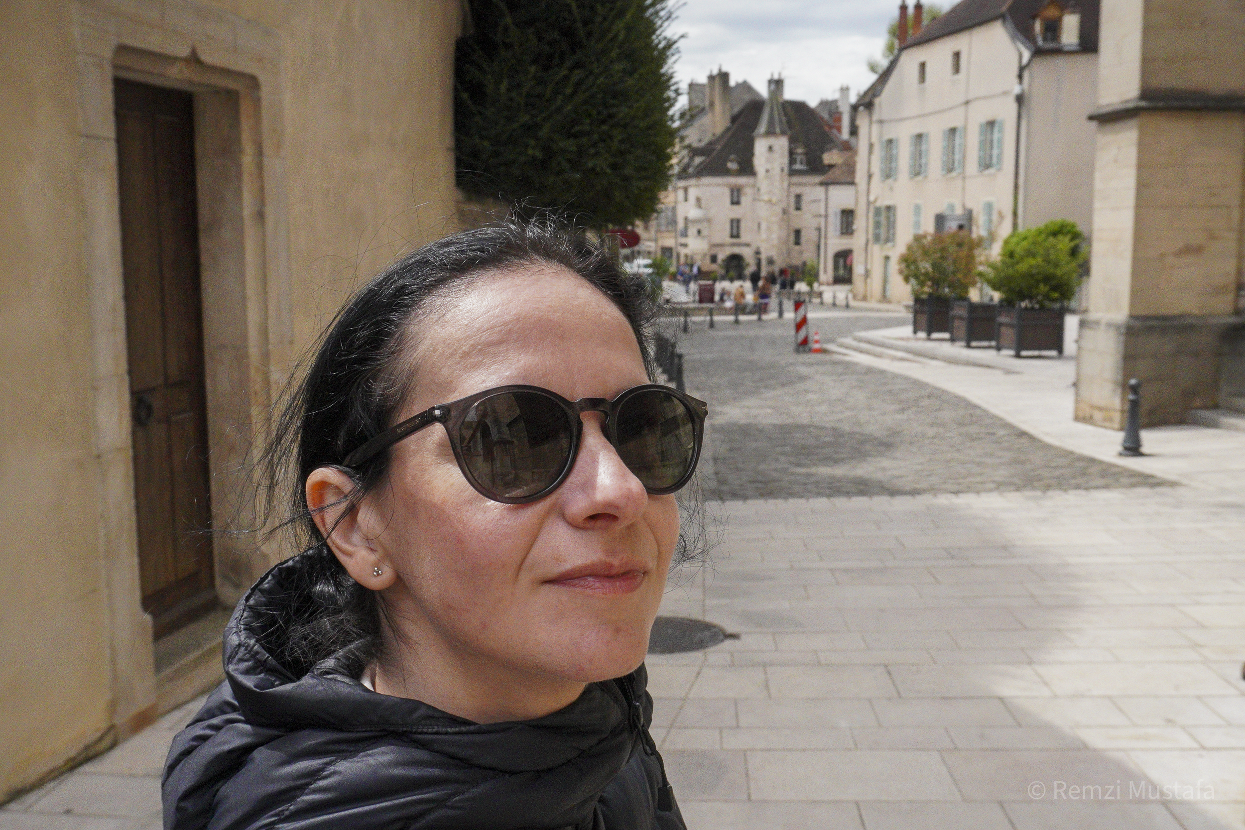 Woman with black hair and sunglasses smiling in a scenic European street with historic buildings