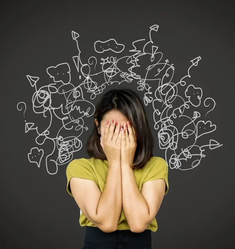 woman with hands over face in front of blackboard with chalk drawings of tangled lines around head