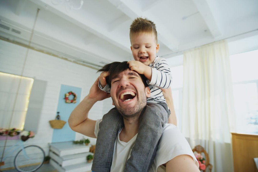 happy-father-carrying-his-smiling-son-on-neck-and-making-selfie-on-smartphone-in-bedroom