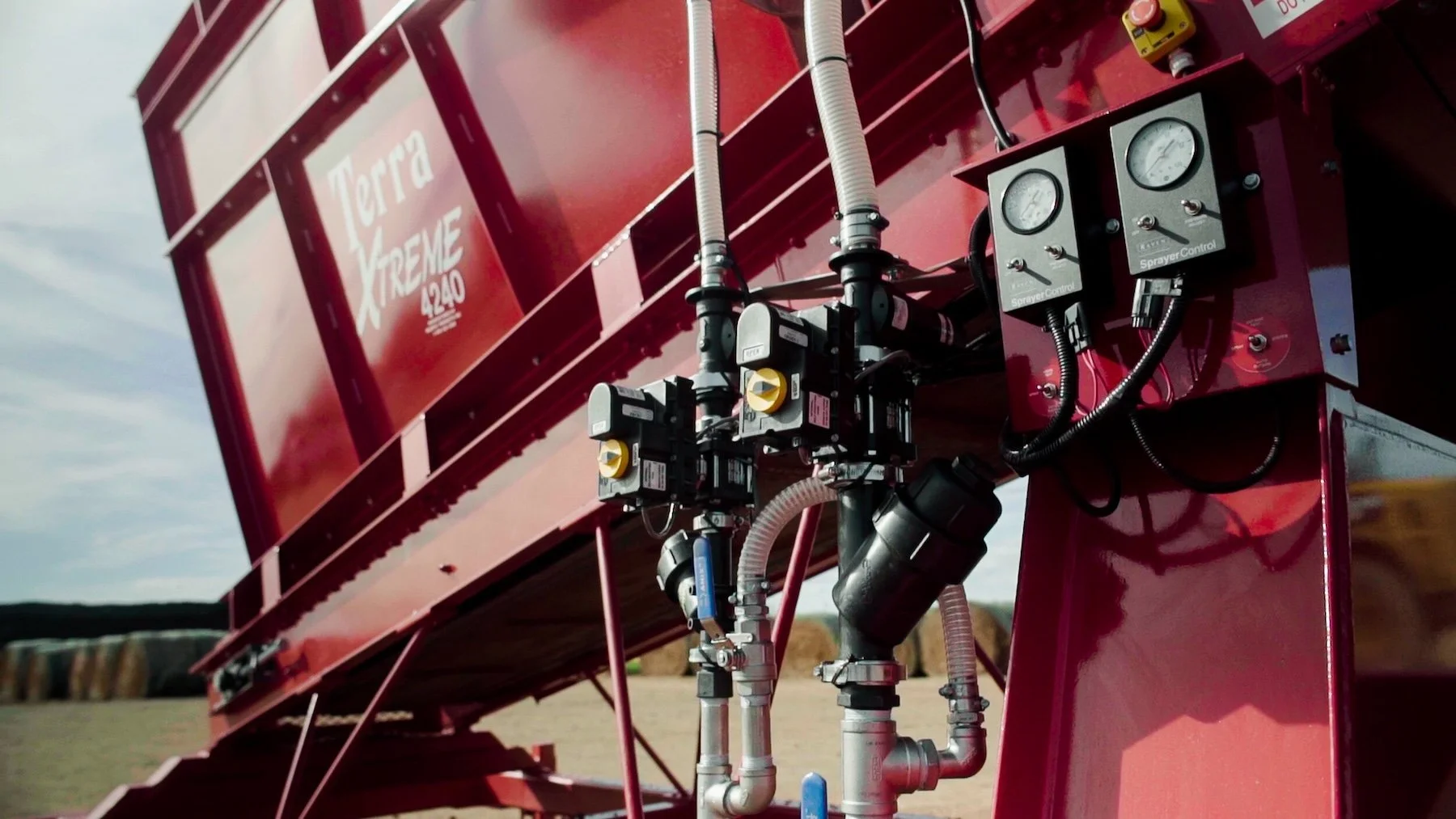 Close-up of a red liquid fertilizer sprayer system labeled 'Terra Xtreme 1240', including pipes, valves, and gauges, outdoors in a field.