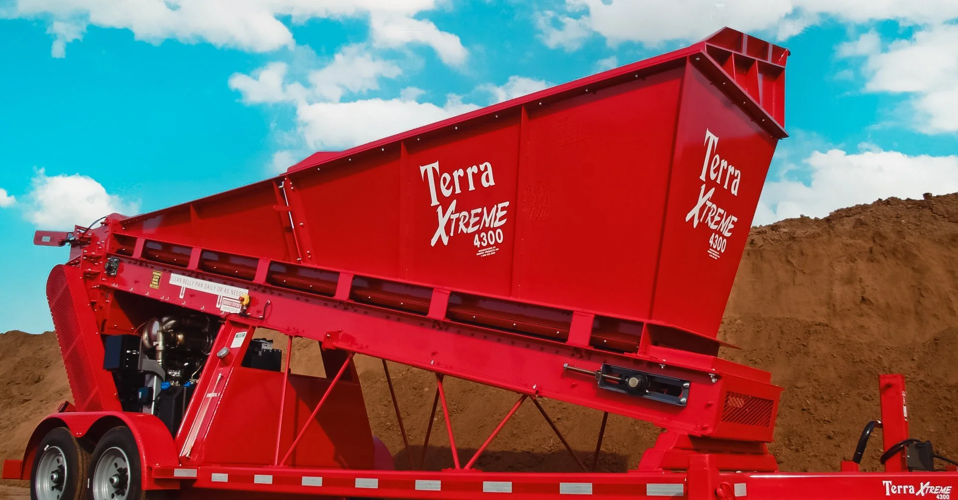 Red Terra Xtreme 4300 soil screening machine on a trailer against a background of brown dirt and partly cloudy blue sky.
