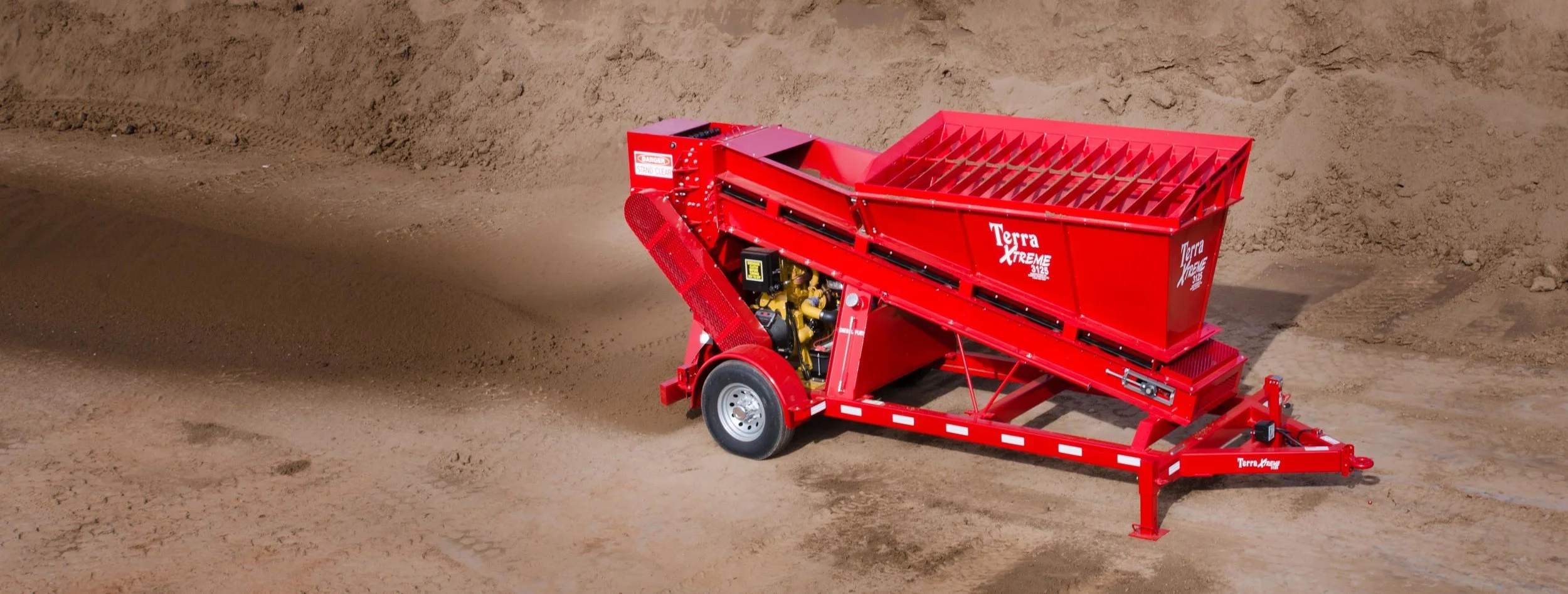 Red gravel plant or screening equipment on a dirt surface at a construction site.