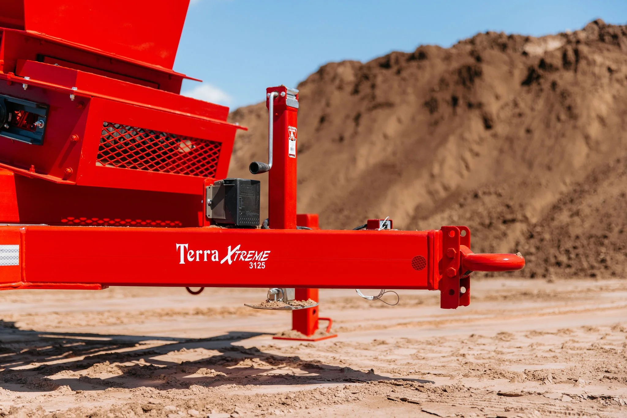Close-up of a red Terra XTREME 3125 trenching machine on sandy terrain with a brown dirt mound in the background.