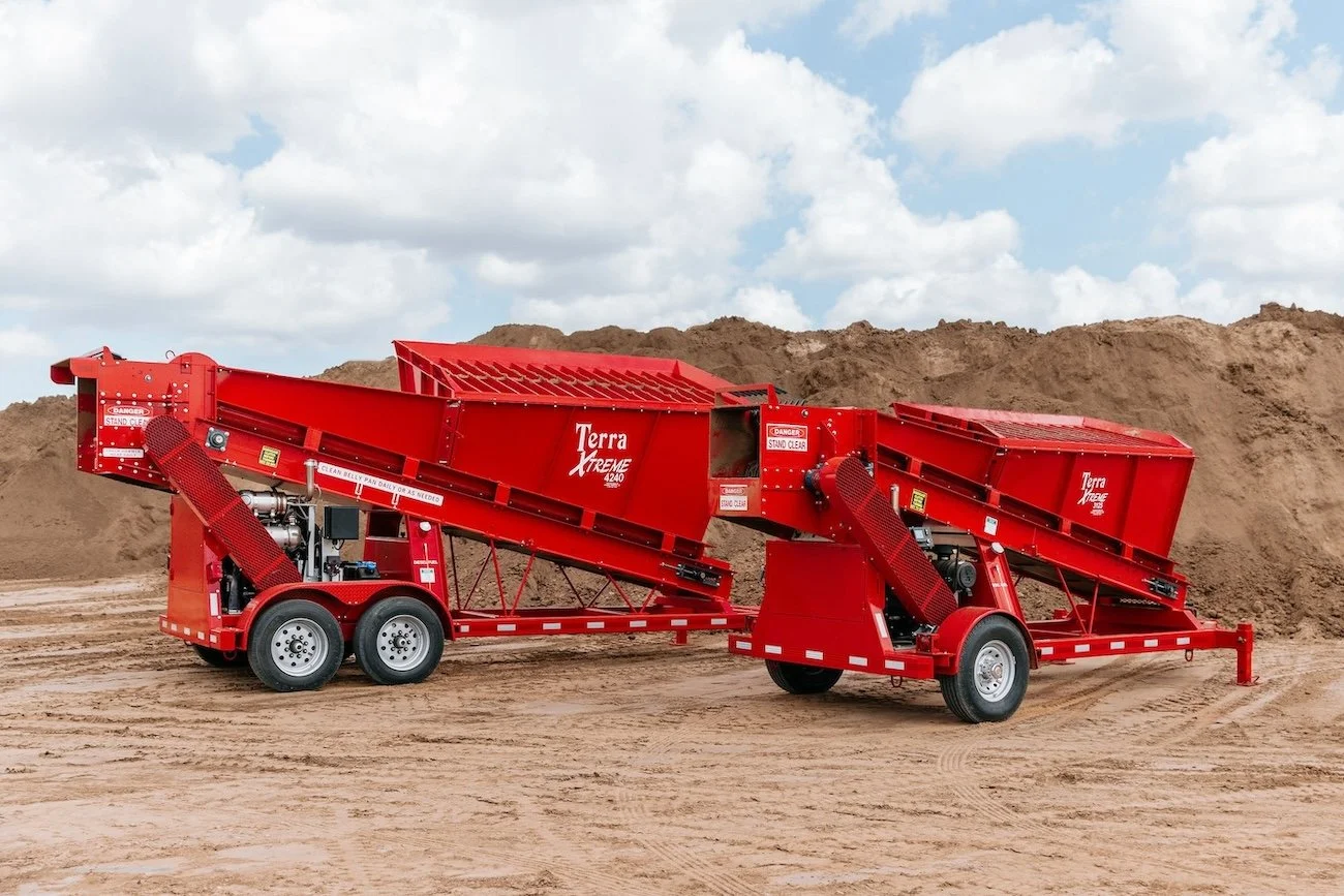 Two red Terra Xtreme mobile rock crushers on a dirt surface with large dirt mounds in the background.