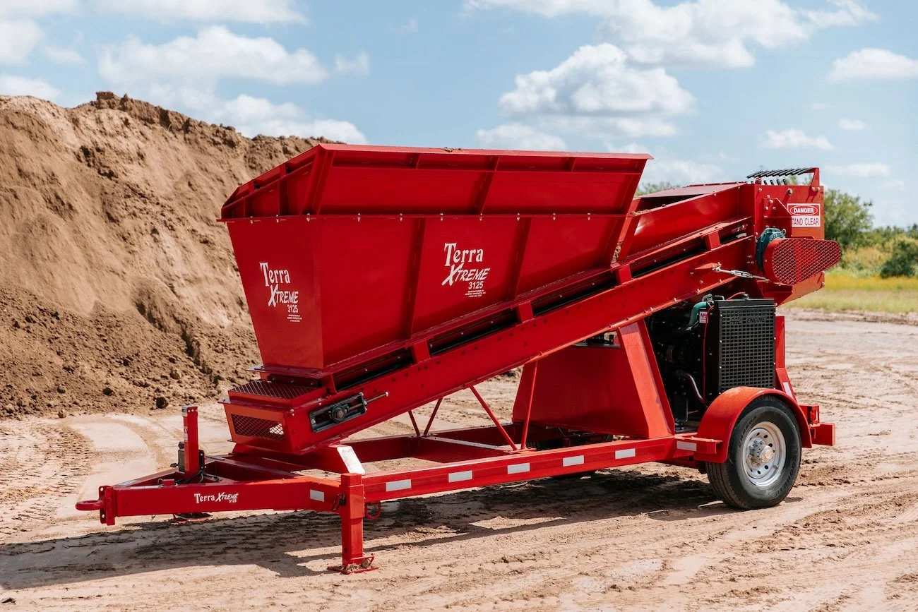Red industrial soil screener on a dirt lot with a large pile of soil in the background.