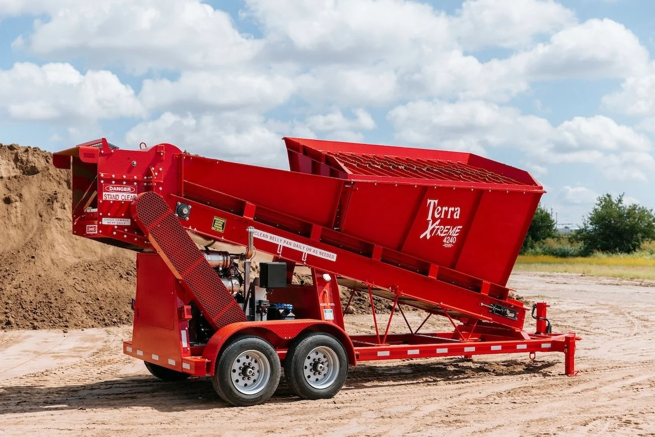 Red Terra Xtreme 4240 soil screener on a trailer in an outdoor construction area with dirt piles and a cloudy sky.