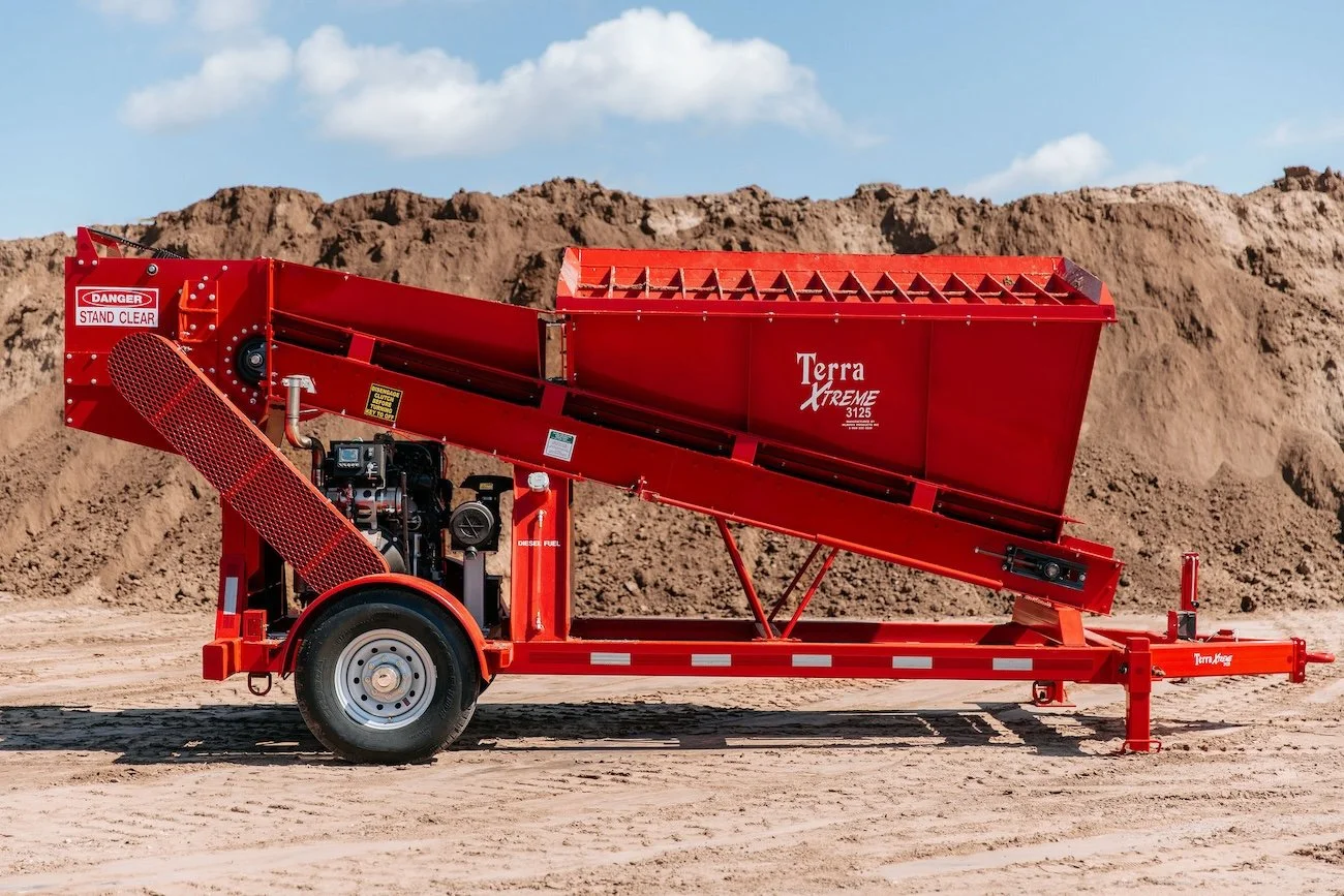 Red Terra Xtreme soil screener on trailer with sandy ground and blue sky.