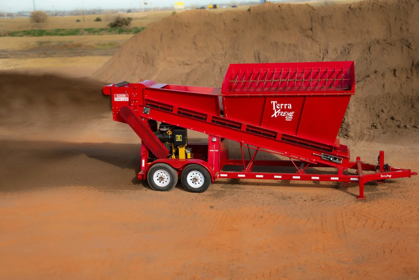 A large red Terra Xtreme industrial soil screener on wheels operating outdoors, sifting dirt on a construction site.