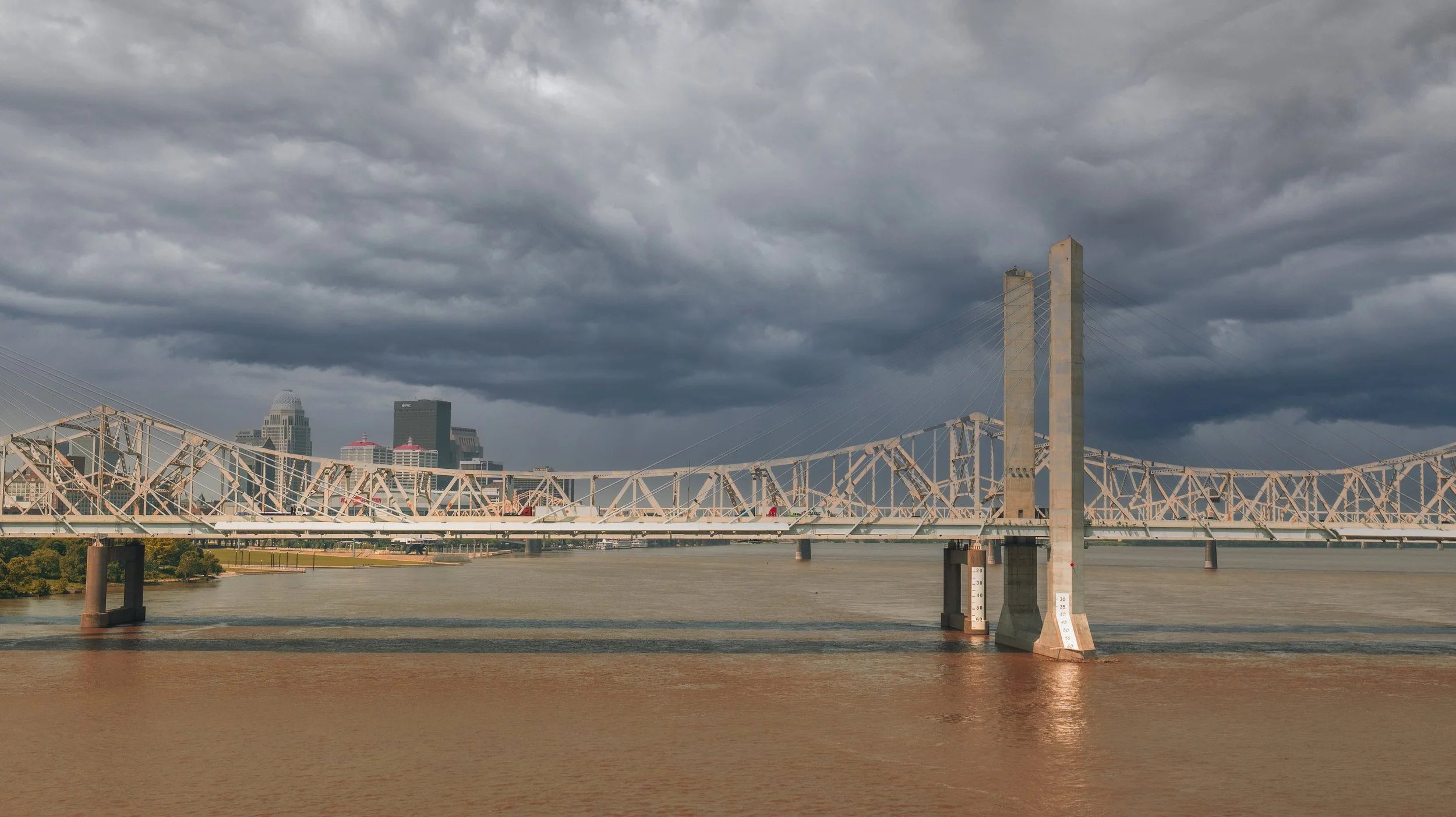 View of a city skyline with a bridge over a river under a cloudy sky.
