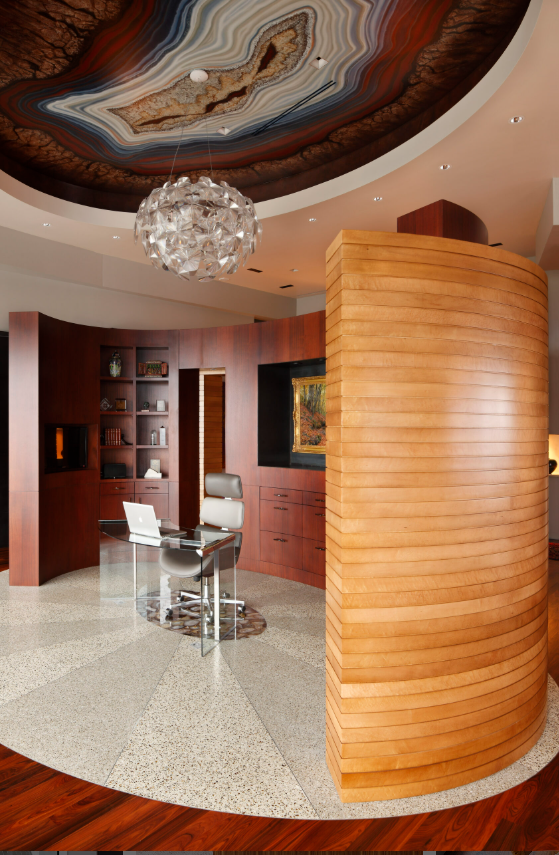 Interior of a modern free floating office within a penthouse with a curved wooden wall, a glass desk, a white office chair, a built-in wooden bookshelf, and a decorative ceiling with a swirling agate design and a spherical chandelier.