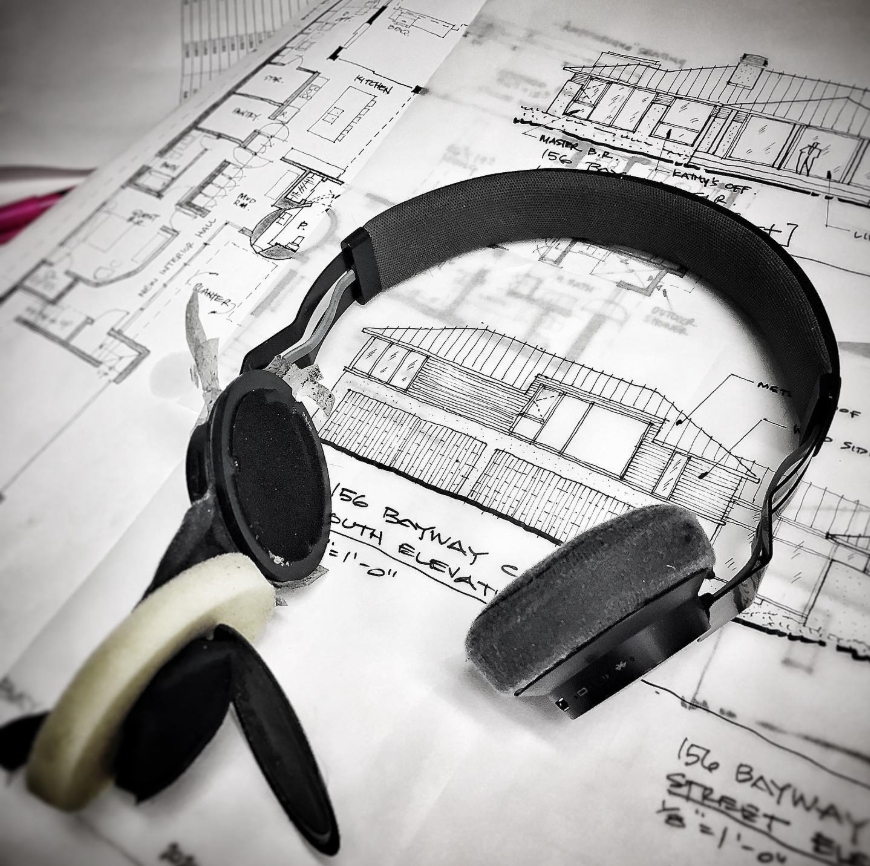 Blueprints and architectural drawings for a building layout with a pair of black headphones placed on top.