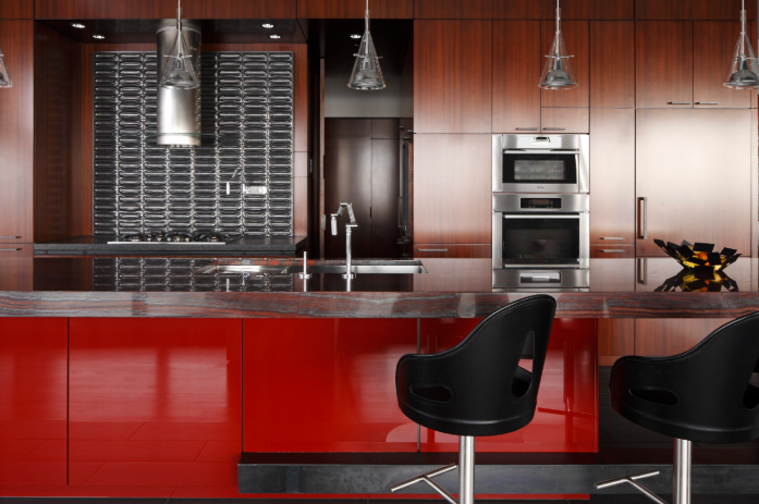 Modern penthouse kitchen with red lacquered wood cabinetry, stainless steel appliances, black barstools, and pendant lighting.